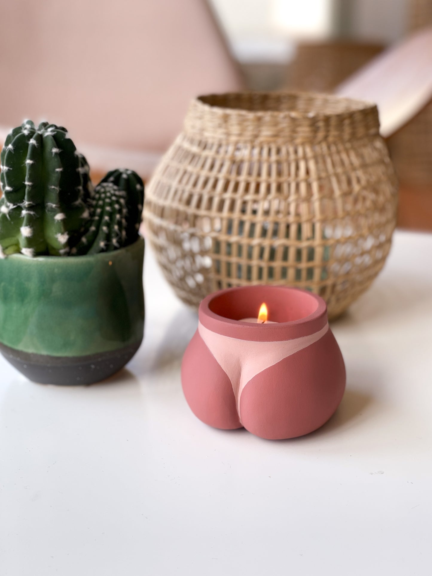 Cache pot Mini Fessier de Maison Tessier, face arrière, fesses, de couleur Bronzé avec une bougie, en mode bougeoir sur une table avec des objets de décoration