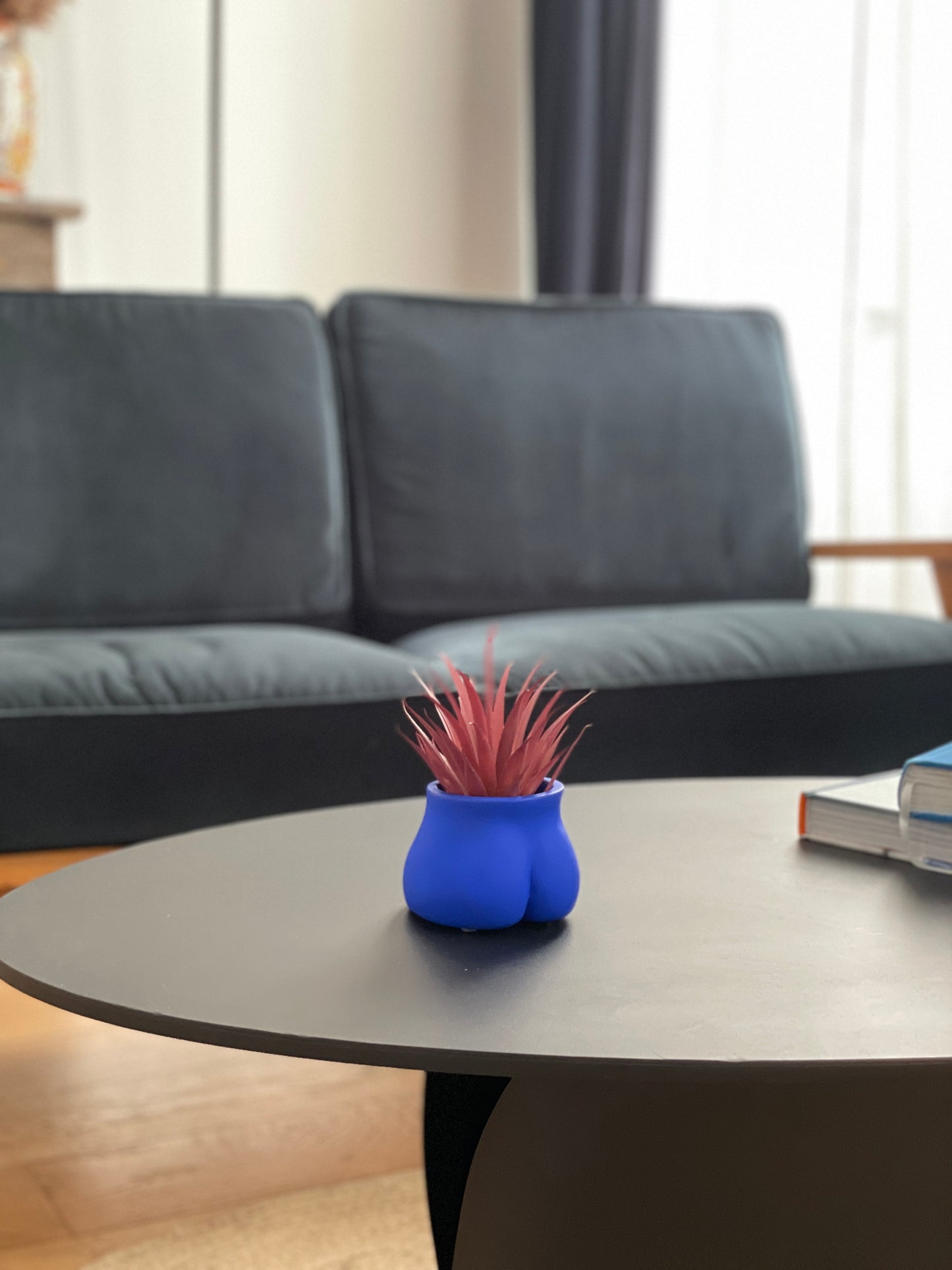 Le Mini Fessier Bleu Klein de Maison Tessier, sur une table basse dans un salon avec une petite plante
