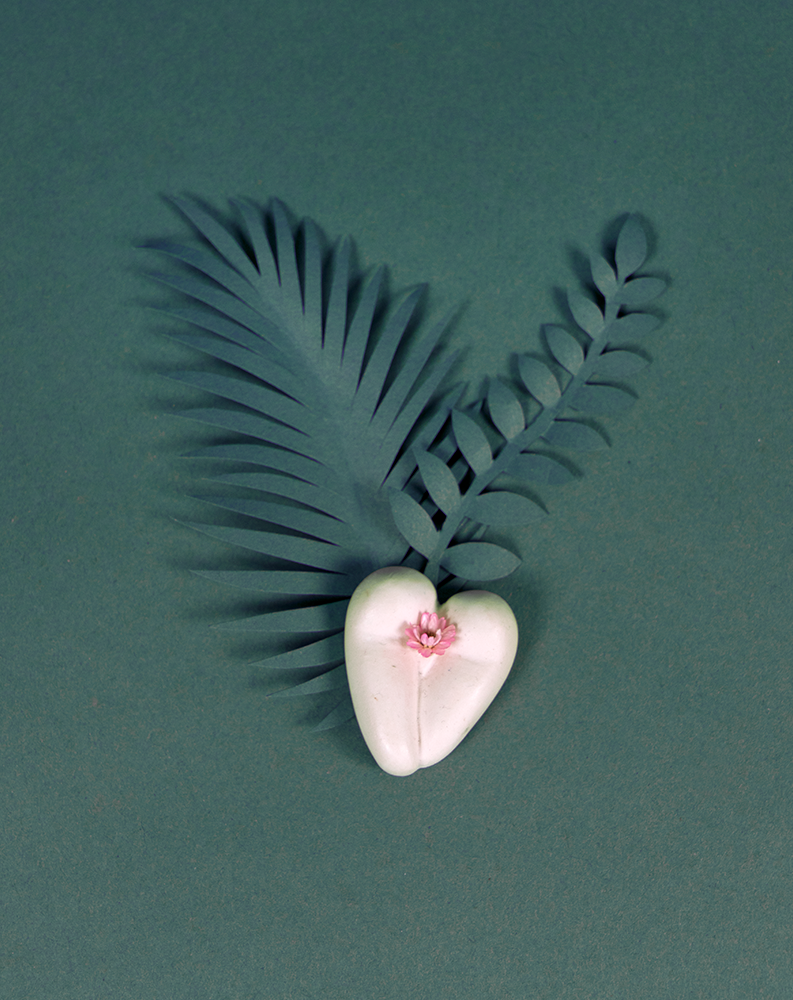 Coeur à nu de Maison Tessier, crème, fesses en forme de coeur avec petite fleur rose, sur fond vert émeraude avec feuilles en papier