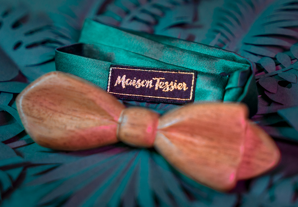 Tour de cou eucalyptus avec un noeud papillon en bois Maison Tessier sur fond de feuilles tropicales en papier, vue de 3/4