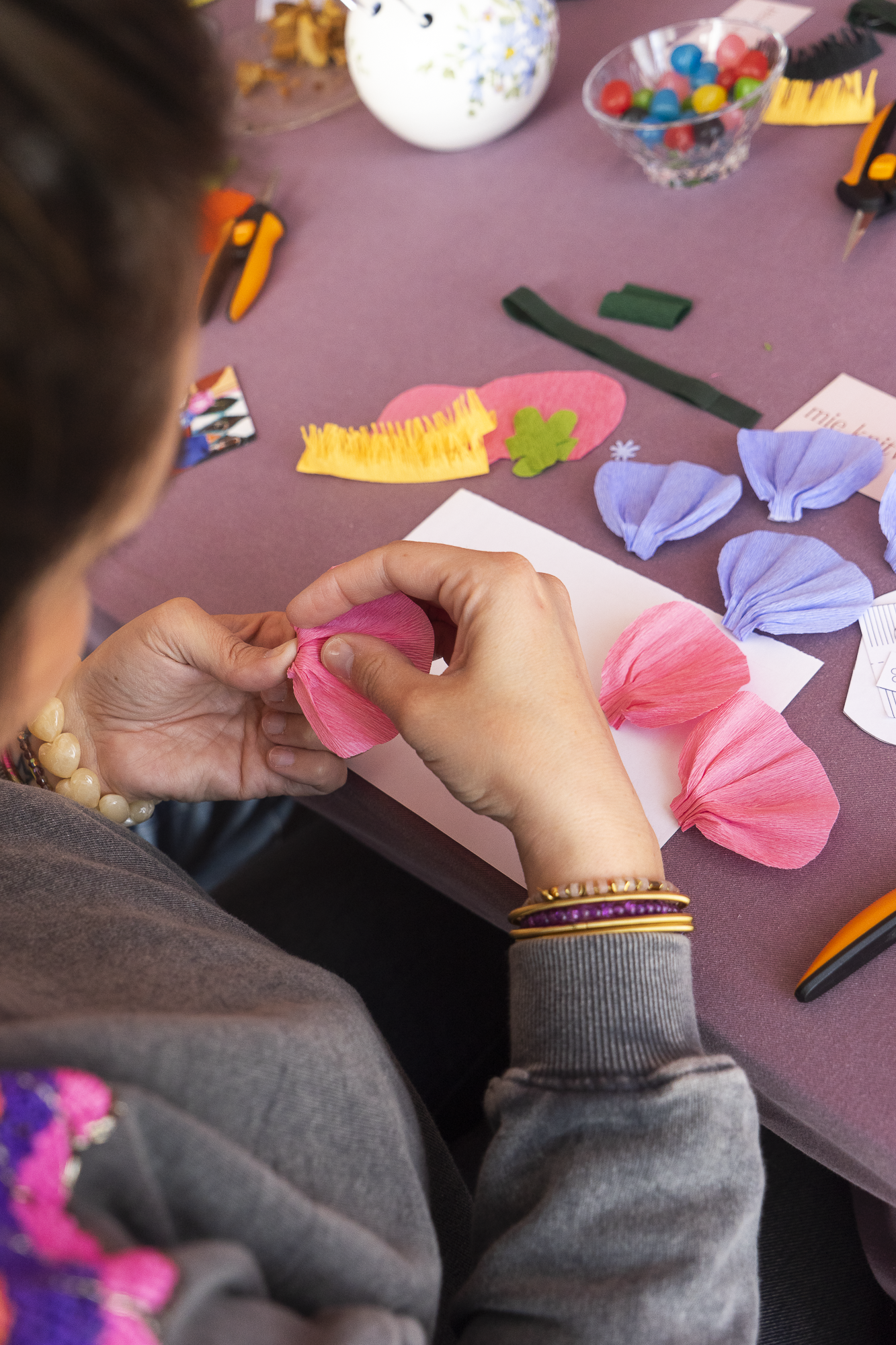 Vue plongeante sur les mains d'une participante façonnant des pétales en papier crépon rose lors d'un atelier fleurs en papier Maison Tessier, atelier créatif, team building, EVJF, animé par Maison Tessier.