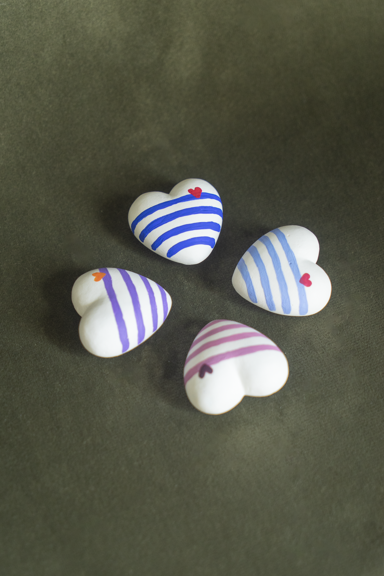 Collection des 4 Magnets Mini Coeur Marinière placés en carré sur un fond vert olive, disponibles en cobalt, en violet, en outremer et en rose, déco parfaite pour un frigo et accrocher vos photos, fabriqués en résine écologique avec amour par Maison Tessier.