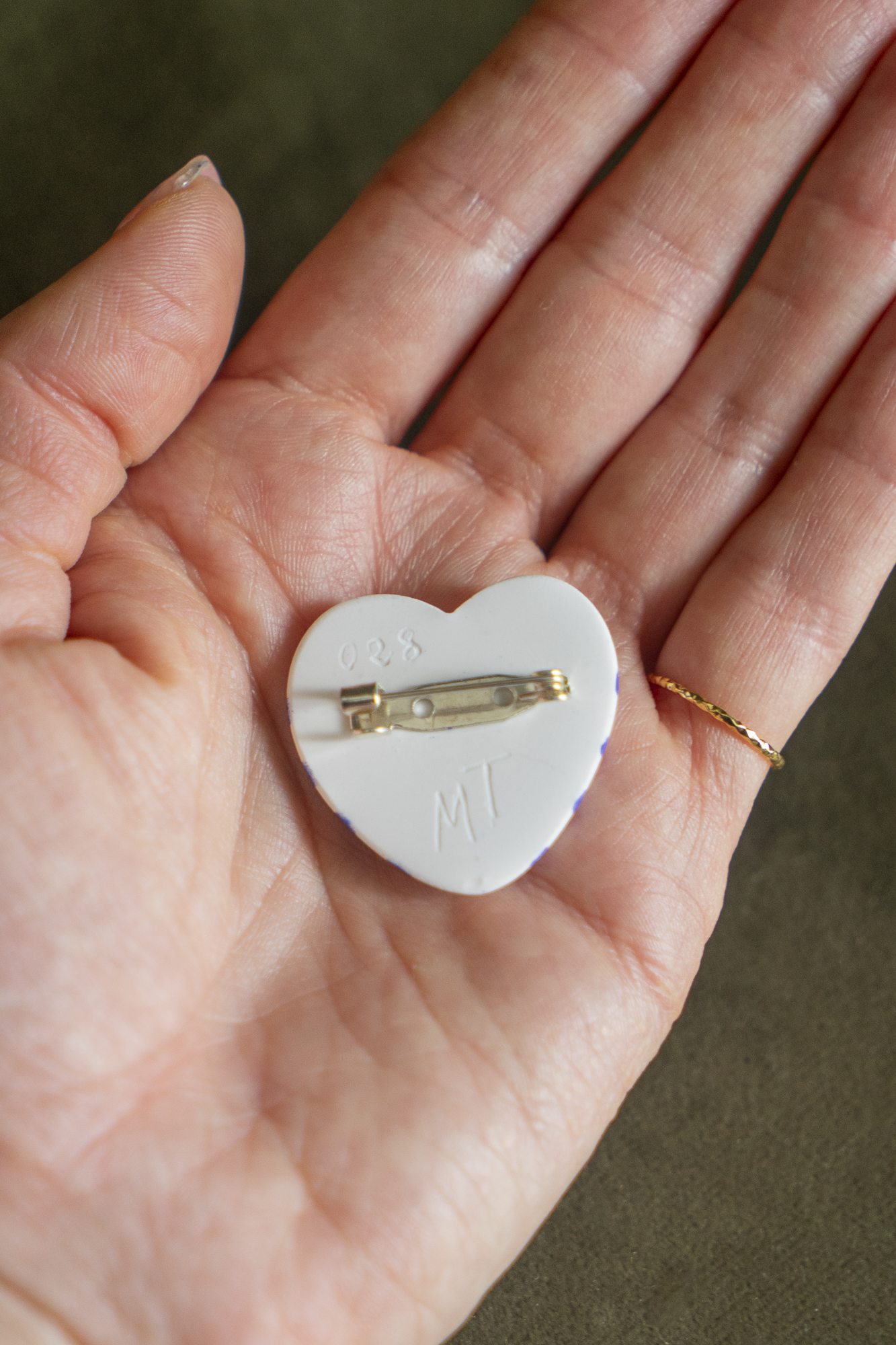 Arrière de la Broche Mini Coeur Marinière Cobalt en résine écologique avec son attache en épingle  et la signature Maison Tessier avec son numéro de série, placée dans une paume de main pour représenter la taille.
