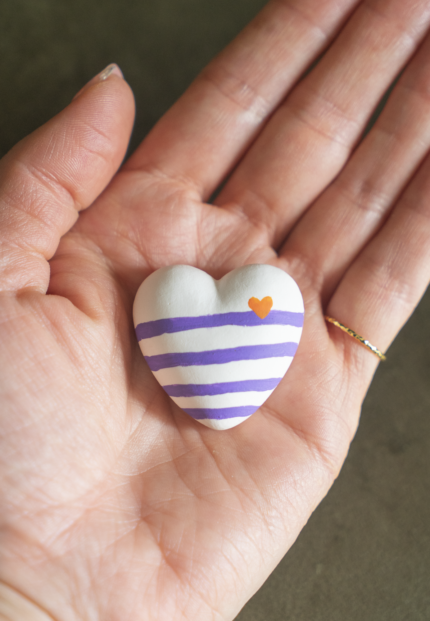 Magnet Mini Cœur Marinière violet en résine écologique, petit coeur bombé avec rayures violettes, avec un petit coeur orange sur la ligne à droite, tenu dans une paume de main pour illustrer sa taille réelle, accessoire déco original et marin fait main par Maison Tessier.