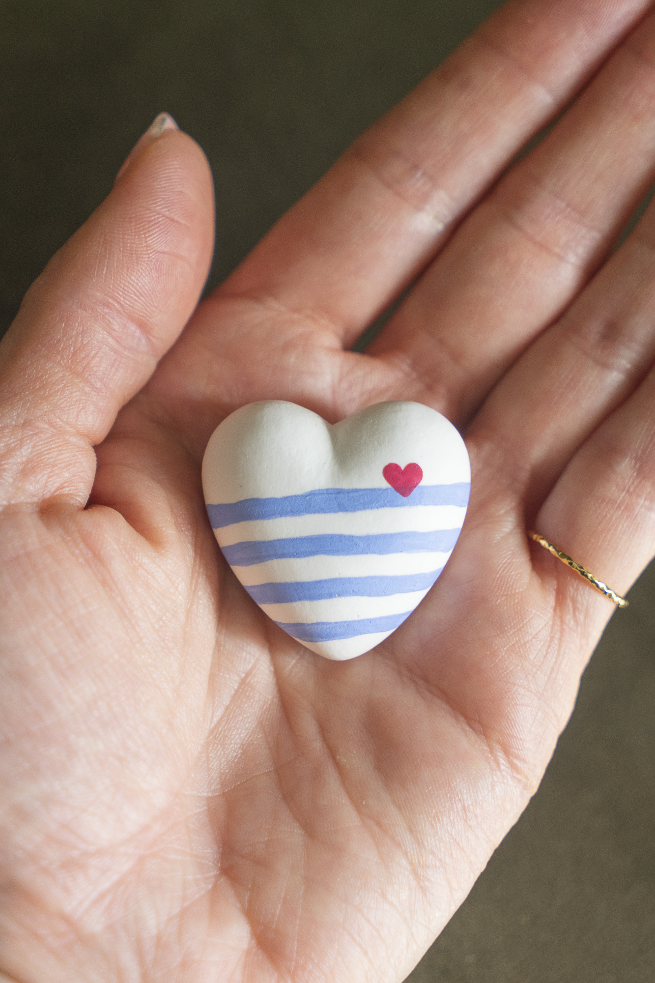 Magnet Mini Cœur Marinière Outremer en résine écologique, petit coeur bombé avec rayures bleu clair, avec un petit coeur rouge sur la ligne à droite, tenu dans une paume de main pour illustrer sa taille réelle, accessoire déco original et marin fait main par Maison Tessier.