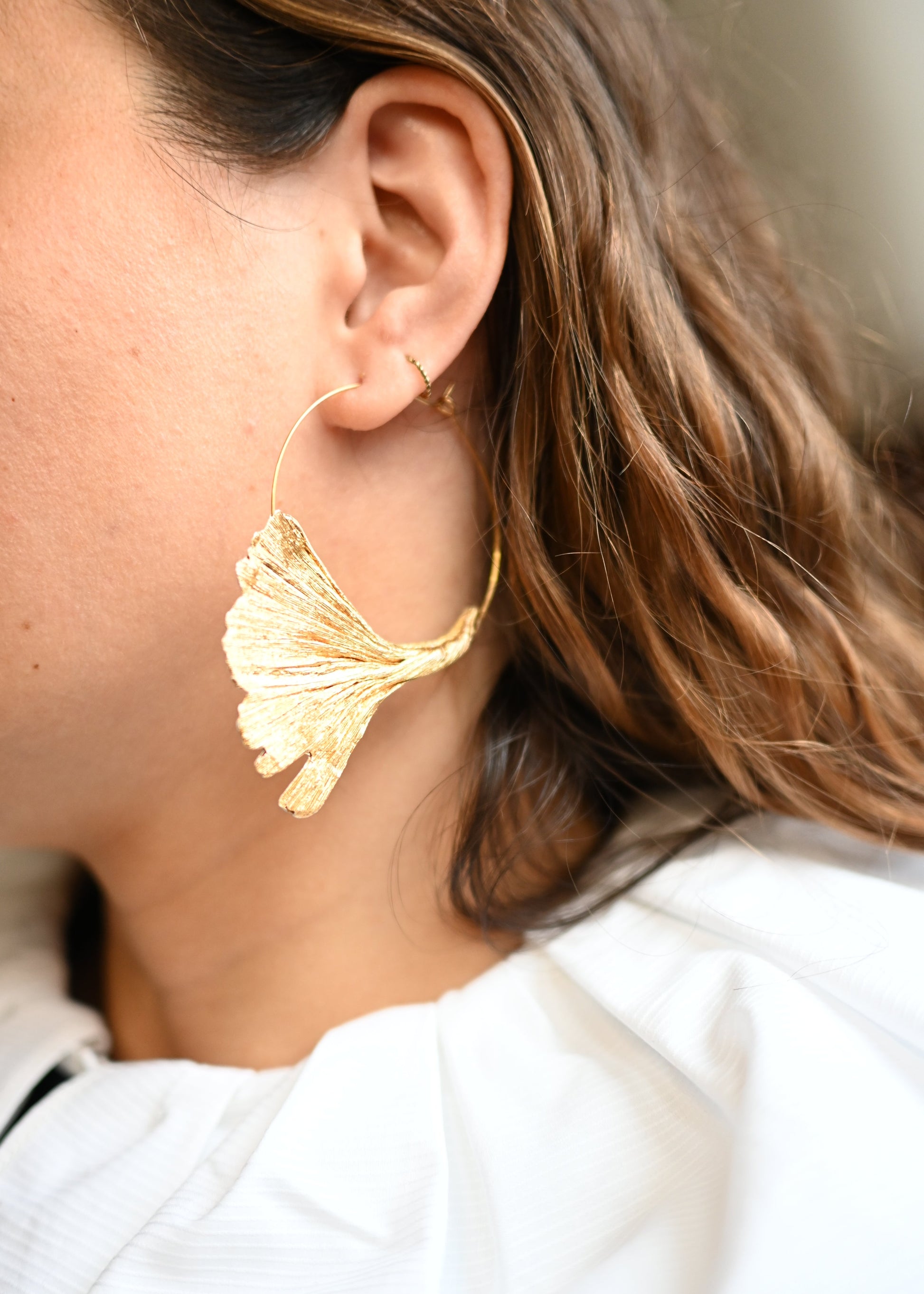 Gros plan sur une femme de profil portant des créoles Ginkgo doré en papier crépon sur anneau doré, boucles d'oreilles artisanales faites main par Maison Tessier.