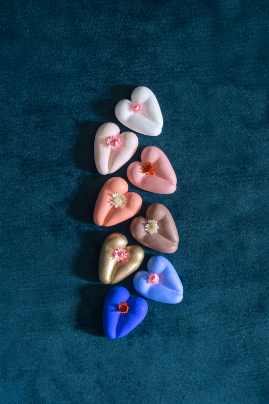 Coeur à nu de Maison Tessier, crème, café, chocolat, terracotta, or, sirène et bleu klein, fesses en forme de coeur avec petites fleurs séchées, sur tissus velour émeraude