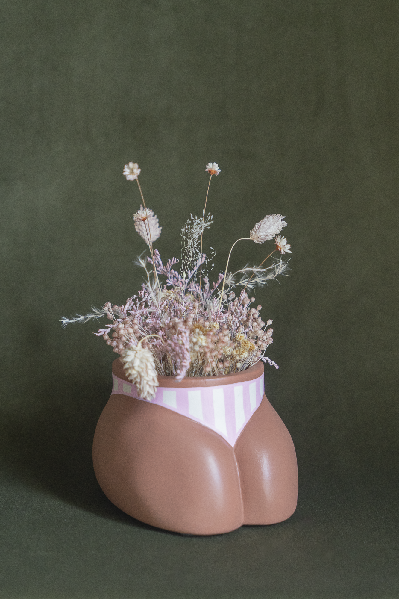 Mini cache-pot Fessier en résine écologique, côté pubis, couleur peau avec un maillot rayures rose et blanc garni d'un bouquet de fleurs séchées avec lagures, gypsophiles, glixias, phalaris rose poudré et blanches sur fond kaki, objet déco floral original fait main par Maison Tessier