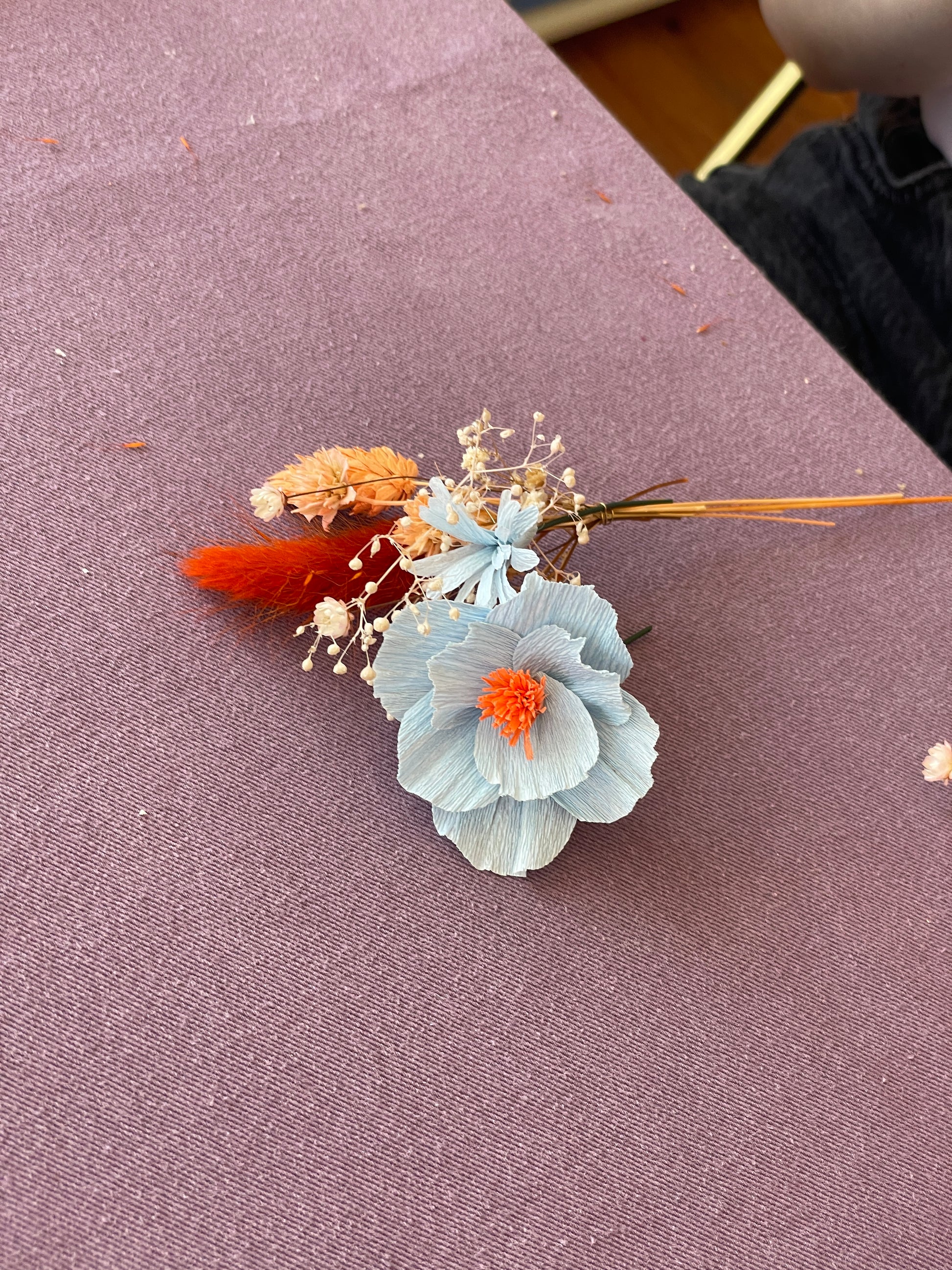 Zoom sur un mini bouquet composé d’une fleur en papier bleu clair avec un coeur orange vif et de fleurs séchées dorées et orangées, atelier EVJF à faire avec ses demoiselles d'honneur, team building, animé par Maison Tessier.