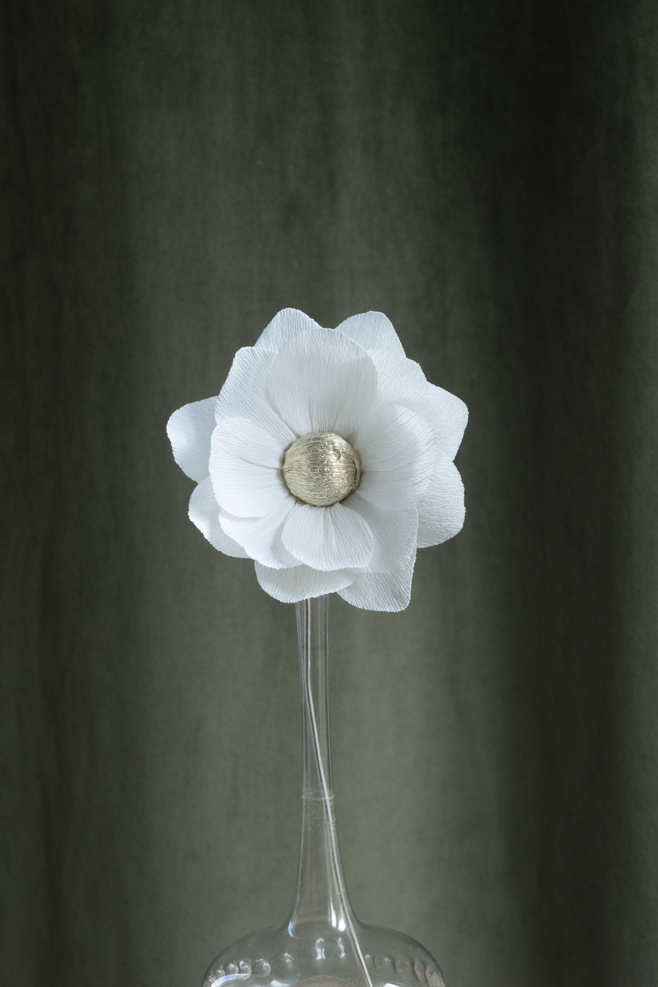 décoration florale faite à la main par Maison Tessier, fleur en papier Nymphea, de couleur blanche au coeur argent, présentée dans un vase en verre transparent, sur fond d'un tissus velour vert kaki