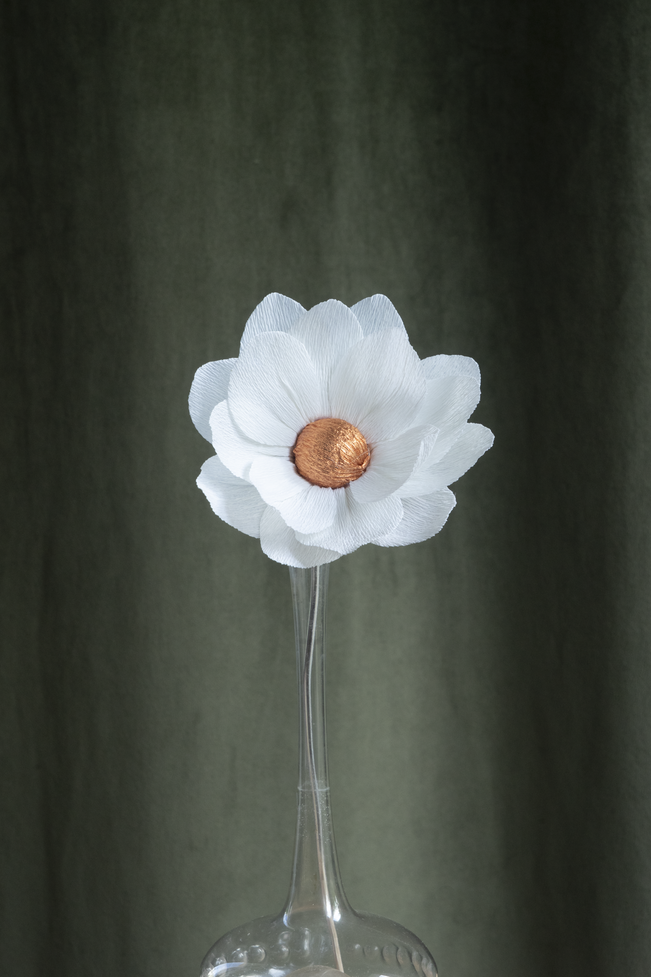 décoration florale faite à la main par Maison Tessier, fleur en papier Nymphea, de couleur blanche au coeur cuivre, présentée dans un vase en verre transparent, sur fond d'un tissus velour vert kaki
