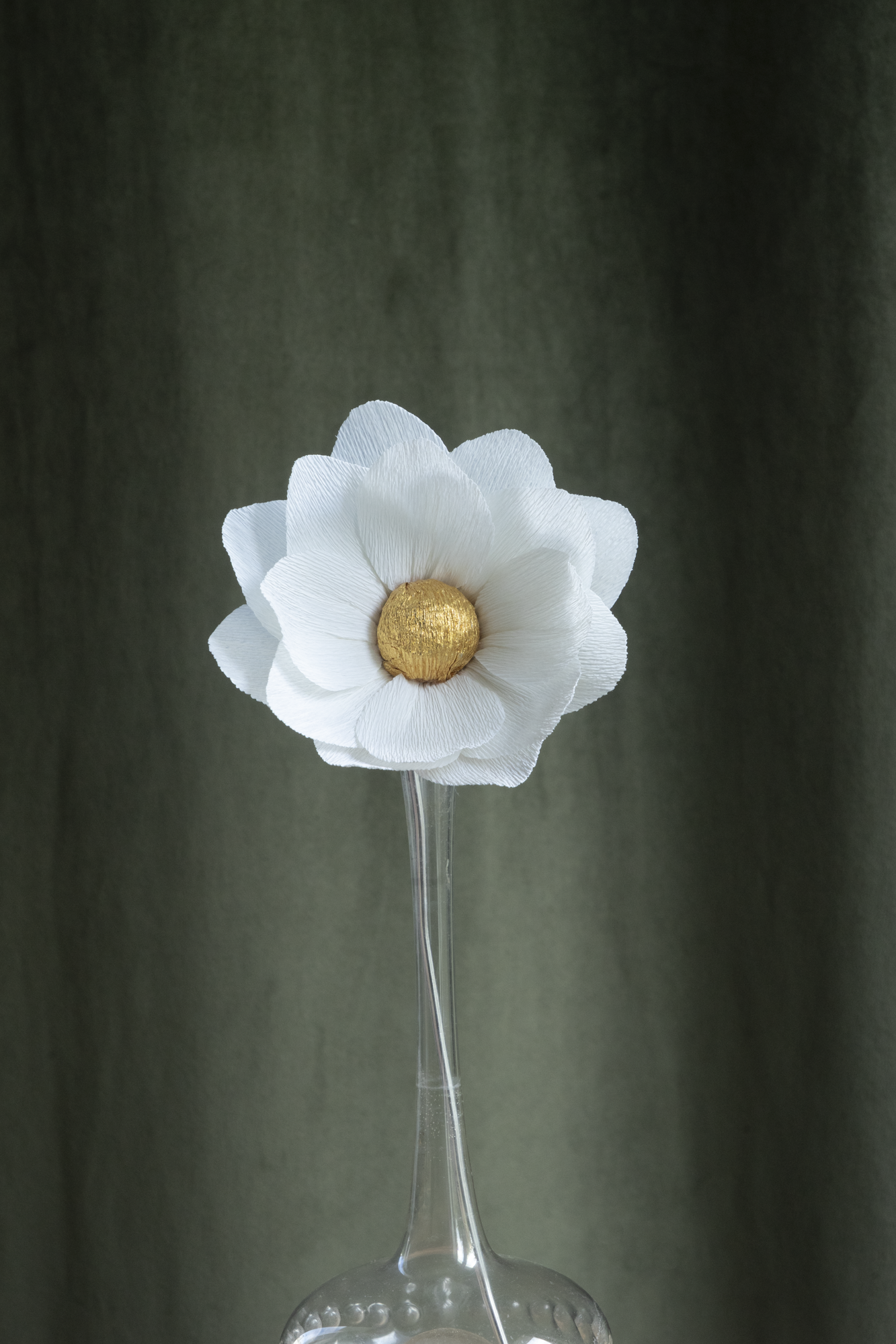 décoration florale faite à la main par Maison Tessier, fleur en papier Nymphea, de couleur blanche au coeur or présentée dans un vase en verre transparent, sur fond d'un tissus velour vert kaki