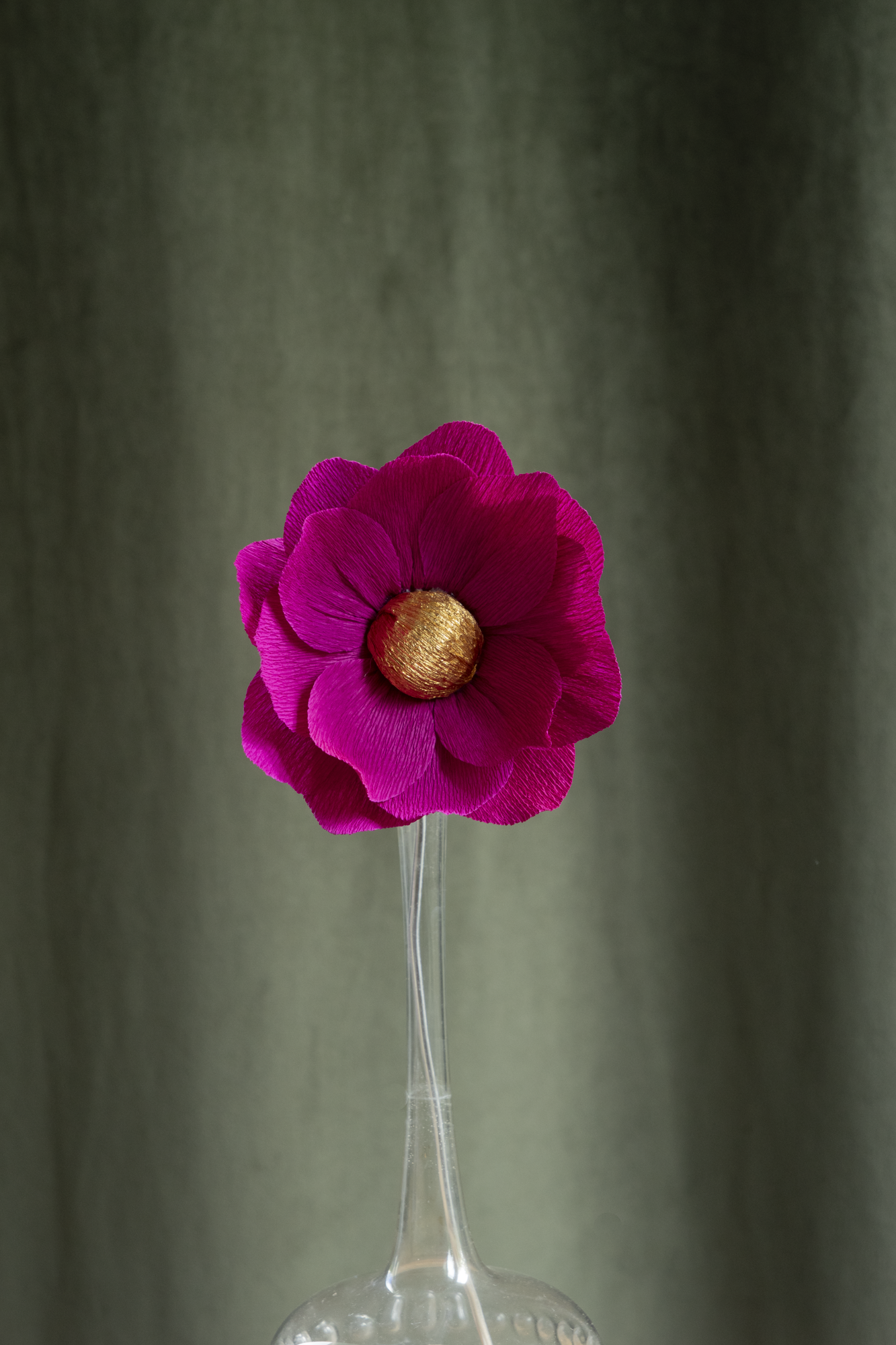 décoration florale faite à la main par Maison Tessier, fleur en papier Nymphea, de couleur fushia au coeur or, présentée dans un vase en verre transparent, sur fond d'un tissus velour vert kaki