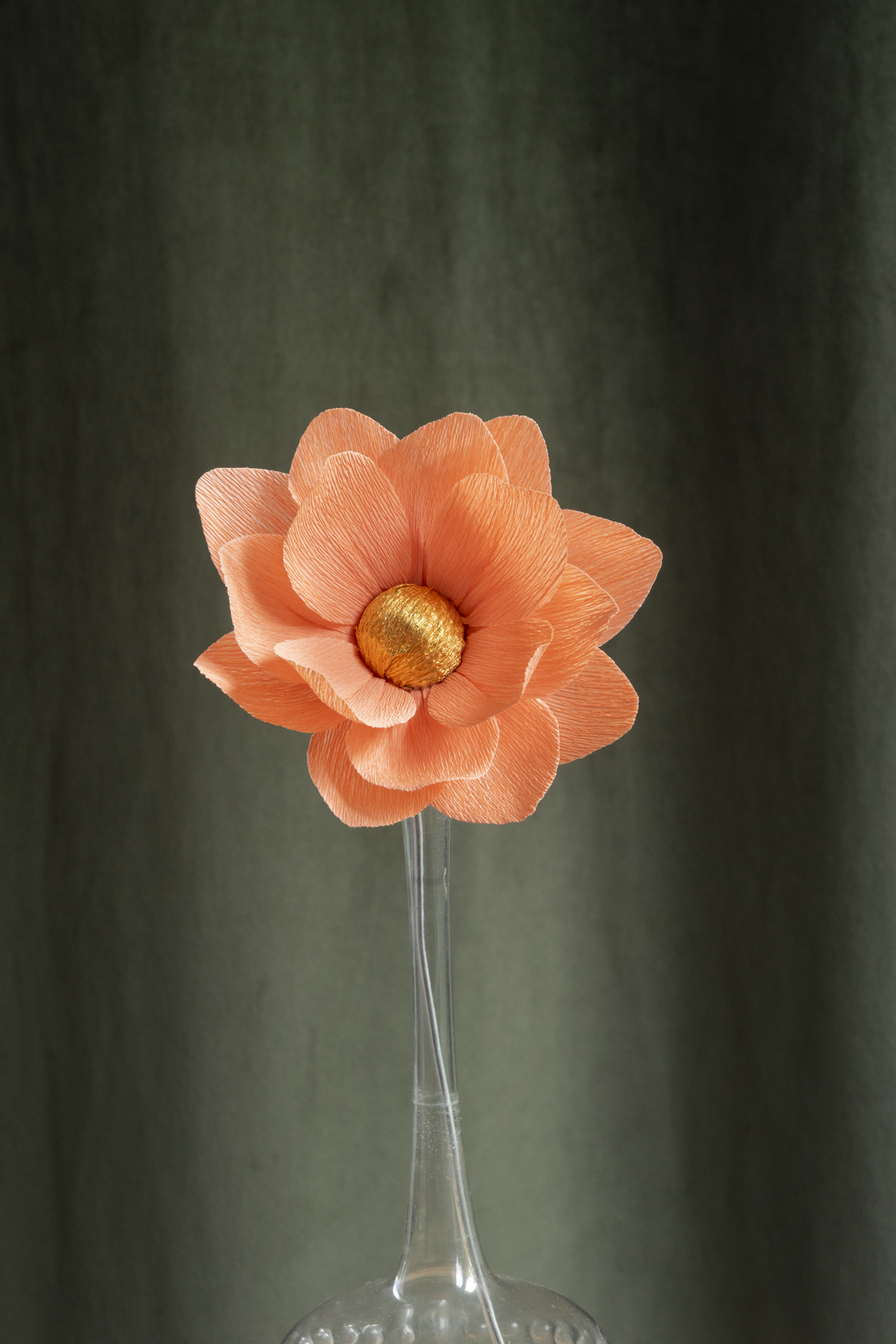 décoration florale faite à la main par Maison Tessier, fleur en papier Nymphea, de couleur orange clair au coeur or, présentée dans un vase en verre transparent, sur fond d'un tissus velour vert kaki