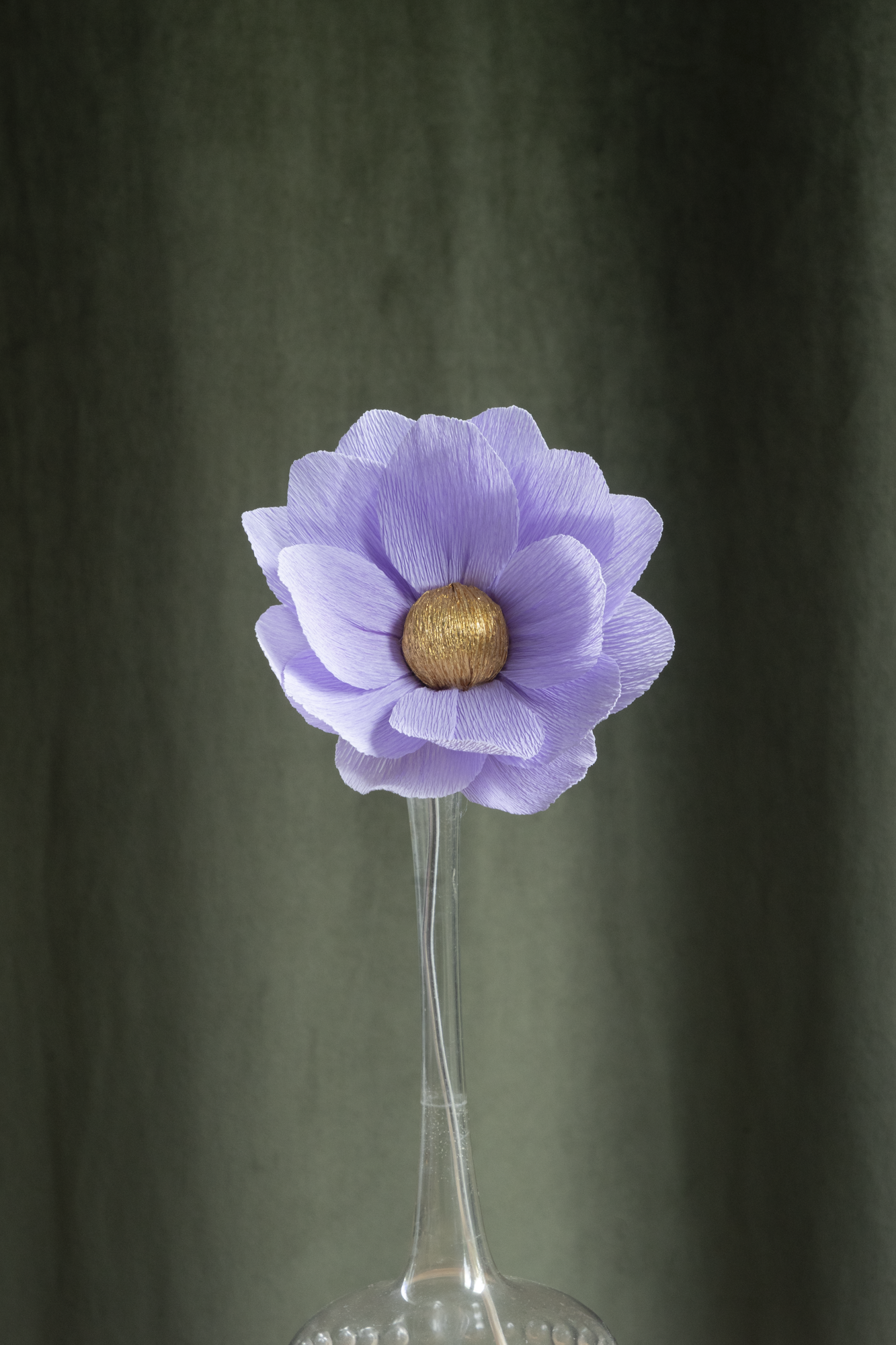 décoration florale faite à la main par Maison Tessier, fleur en papier Nymphea, de couleur parme au coeur or, présentée dans un vase en verre transparent, sur fond d'un tissus velour vert kaki