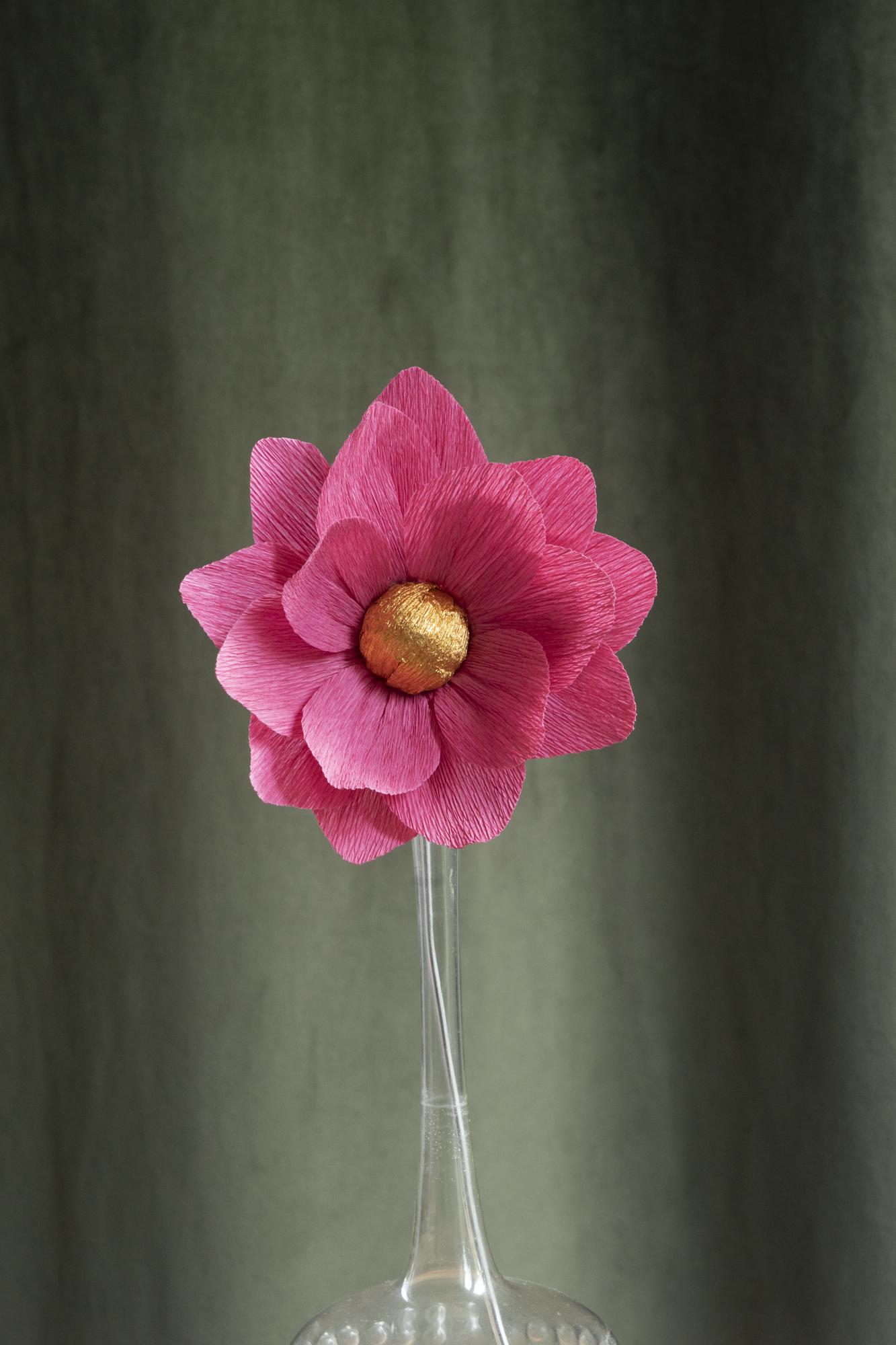 décoration florale faite à la main par Maison Tessier, fleur en papier Nymphea, de couleur rose au coeur or, présentée dans un vase en verre transparent, sur fond d'un tissus velour vert kaki