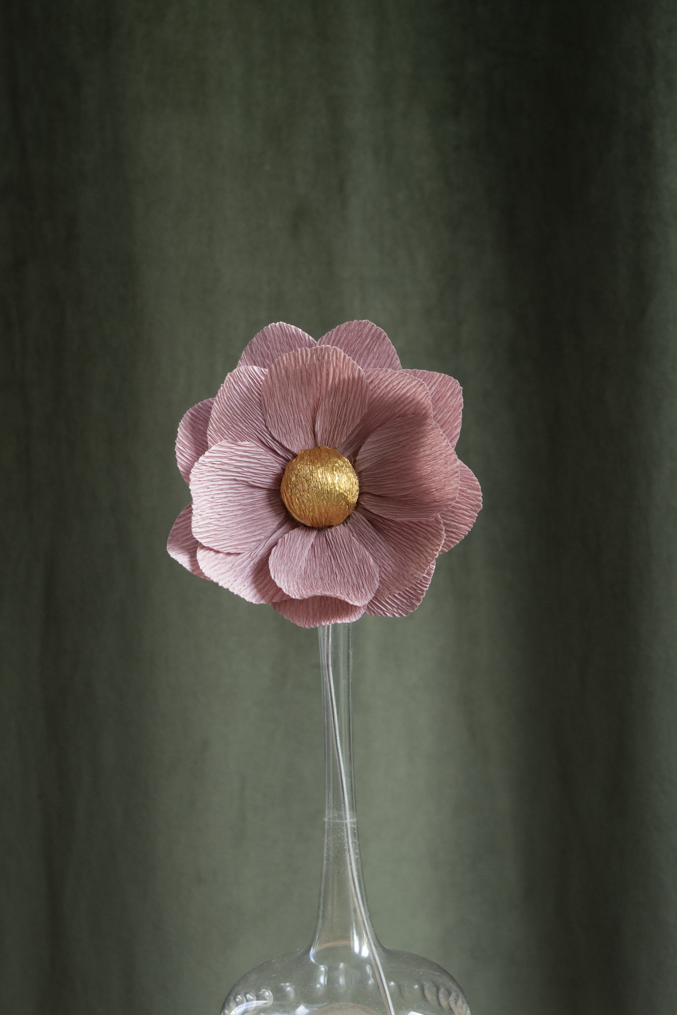décoration florale faite à la main par Maison Tessier, fleur en papier Nymphea, de couleur vieux rose au coeur or, présentée dans un vase en verre transparent, sur fond d'un tissus velour vert kaki