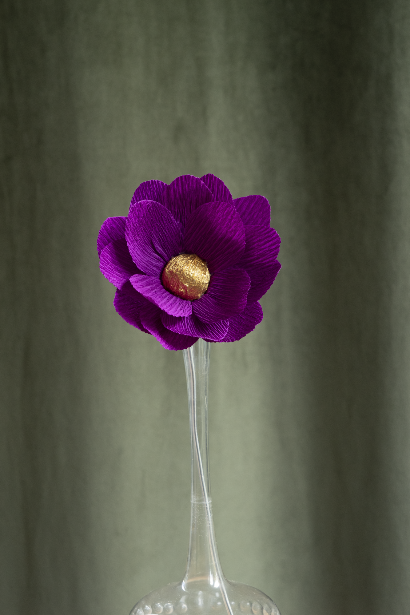 décoration florale faite à la main par Maison Tessier, fleur en papier Nymphea, de couleur violet au coeur or, présentée dans un vase en verre transparent, sur fond d'un tissus velour vert kaki