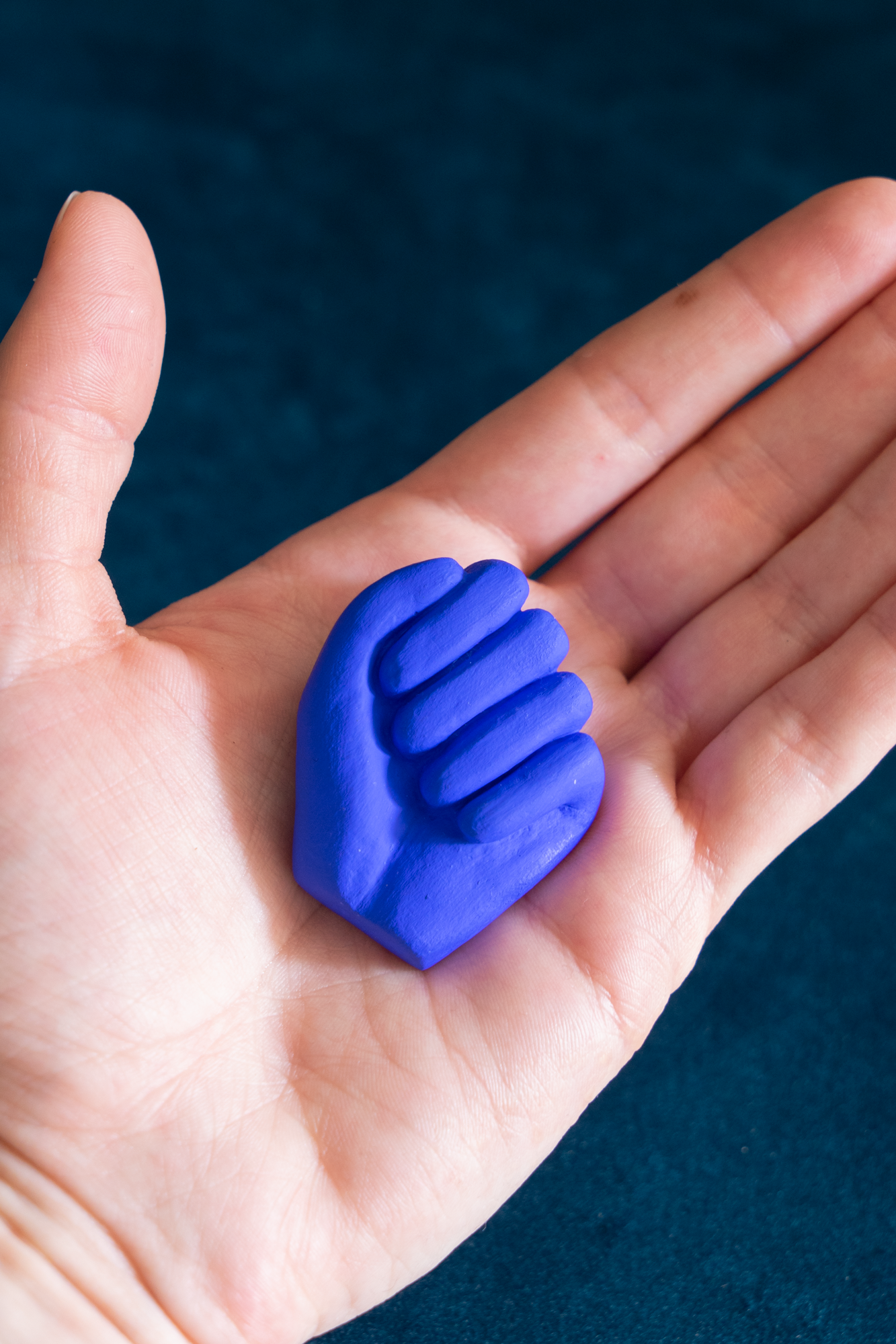 Mini Main Bleu Klein de Maison Tessier, dans une main, sur fond velour vert émeraude