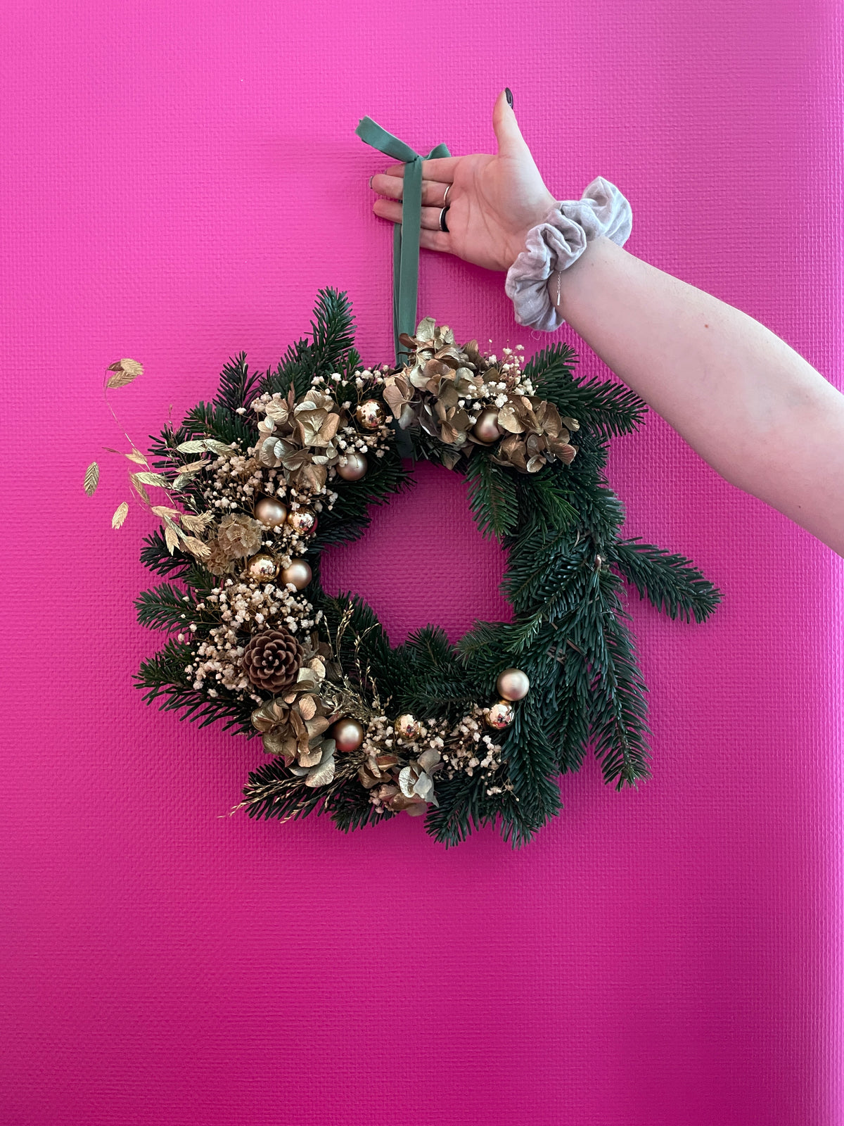 Couronne de noel dorée sur fond rose fushia tenu par une main avec un chouchou