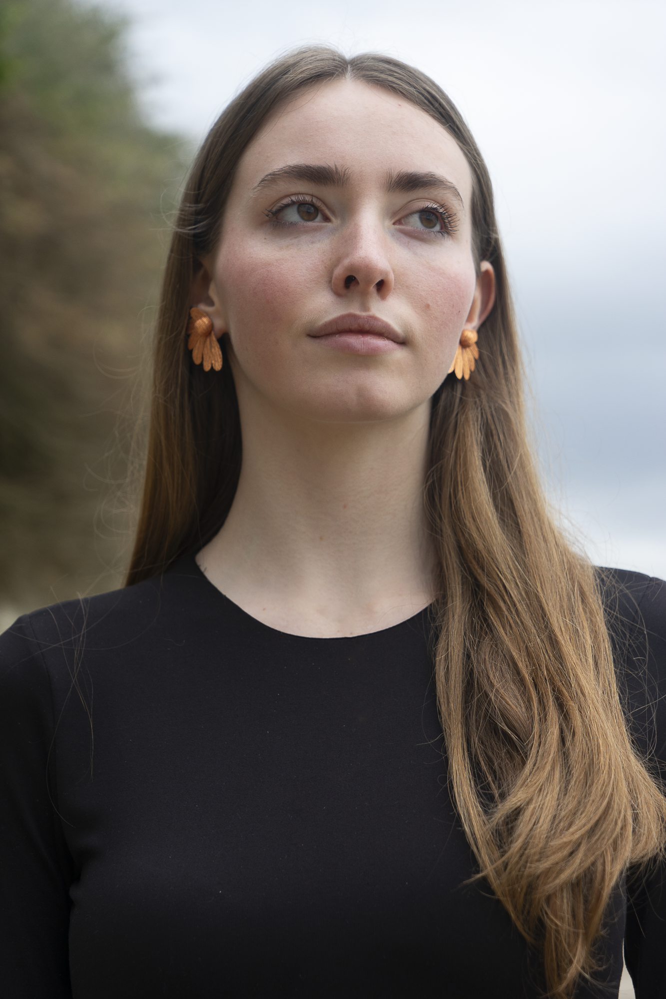 Femme portant des boucles d'oreilles, Puces Pâquerettes cuivre en papier crépon fait main, bijoux floraux artisanaux fabriqués par Maison Tessier
