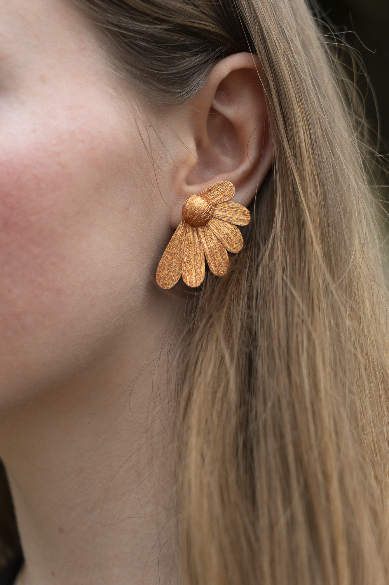  Gros plan sur une boucle d'oreilles Puce Pâquerettes cuivre en papier crépon et cœur cuivre portée à l'oreille, bijoux floraux artisanaux fait main par Maison Tessier.  