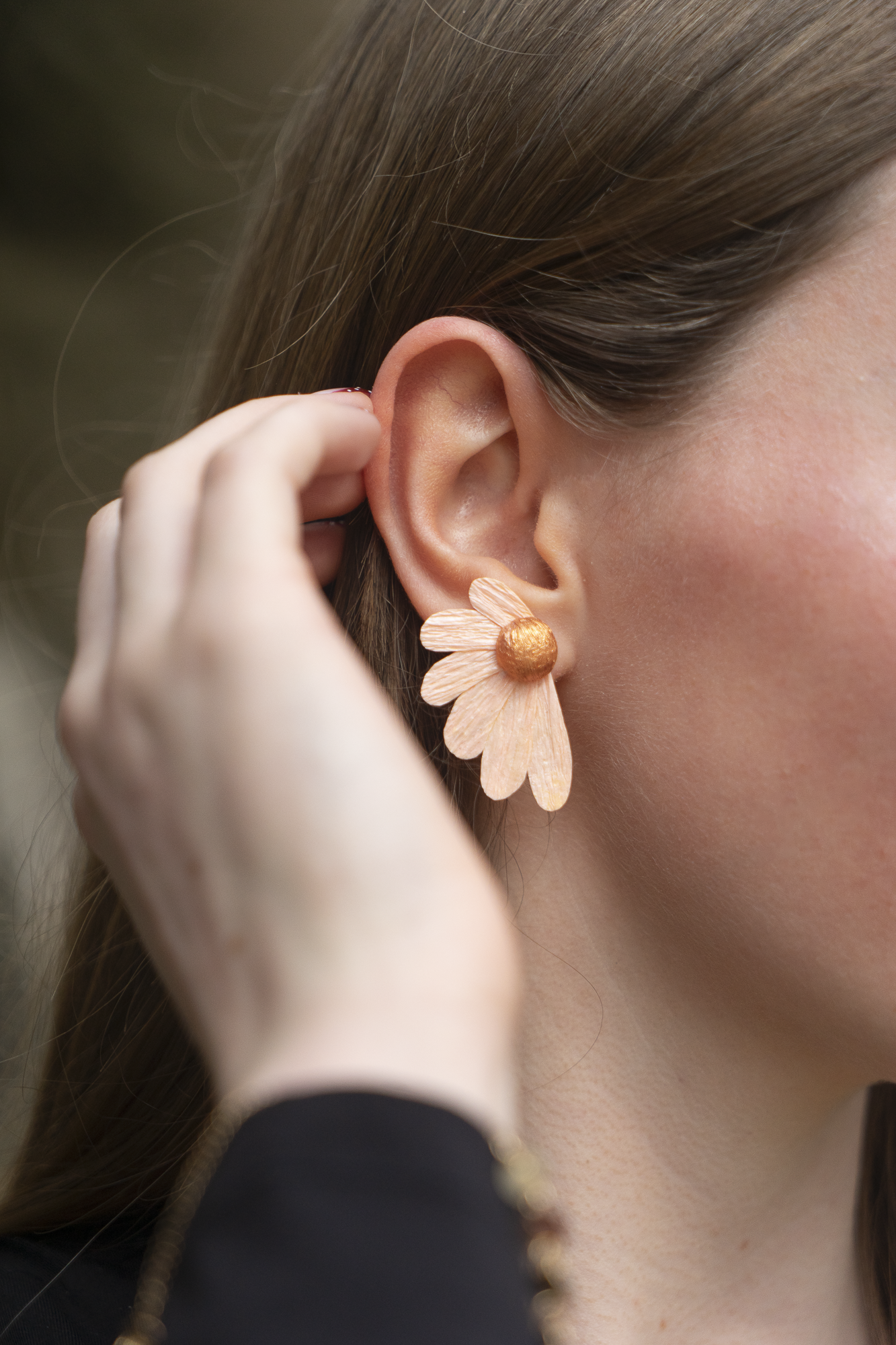Gros plan sur une femme portant une boucle d'oreille Puce Pâquerettes quartz orange, blanc crème en papier crépon et cœur doré portée à l'oreille, bijoux floraux artisanaux faits main par Maison Tessier.