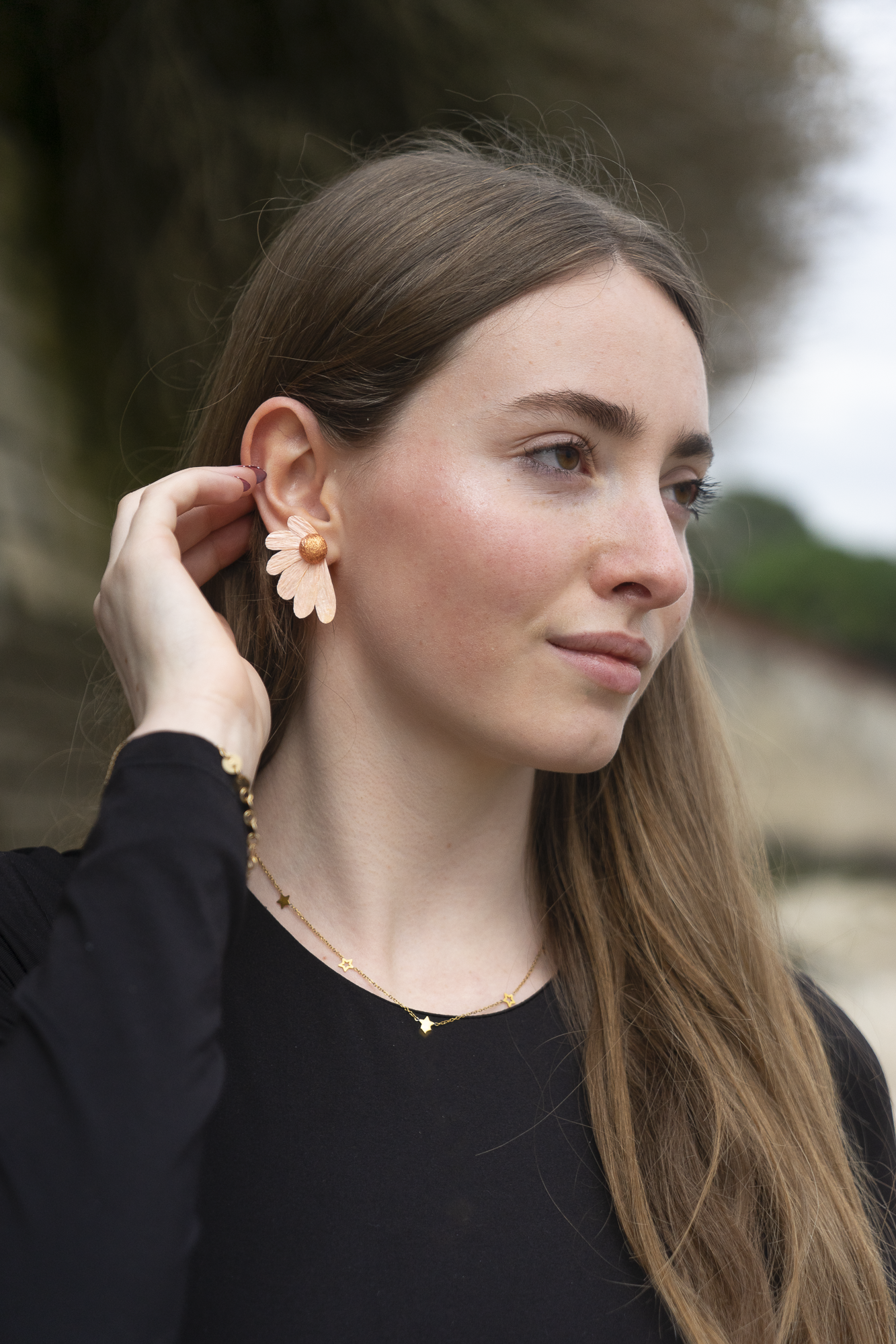 Femme portant des boucles d’oreilles, Puces Pâquerrettes Quartz orange, blanc crème en papier crépon fait main, bijoux floraux artisanaux fabriqués par Maison Tessier.