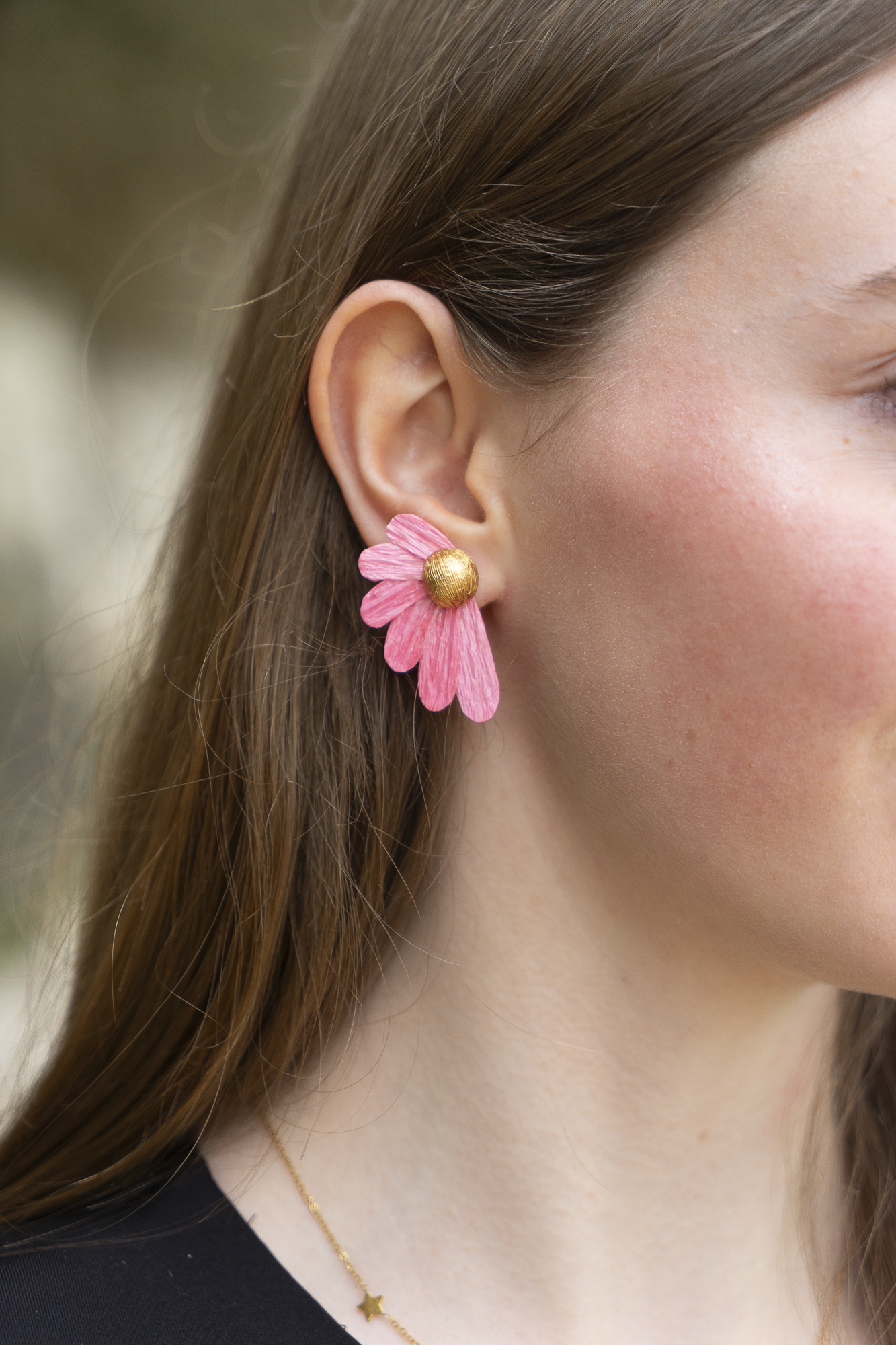 Gros plan sur une femme portant une boucle d'oreilles Puce Pâquerettes rose en papier crépon et cœur doré, bijoux floraux artisanaux faits main par Maison Tessier.
