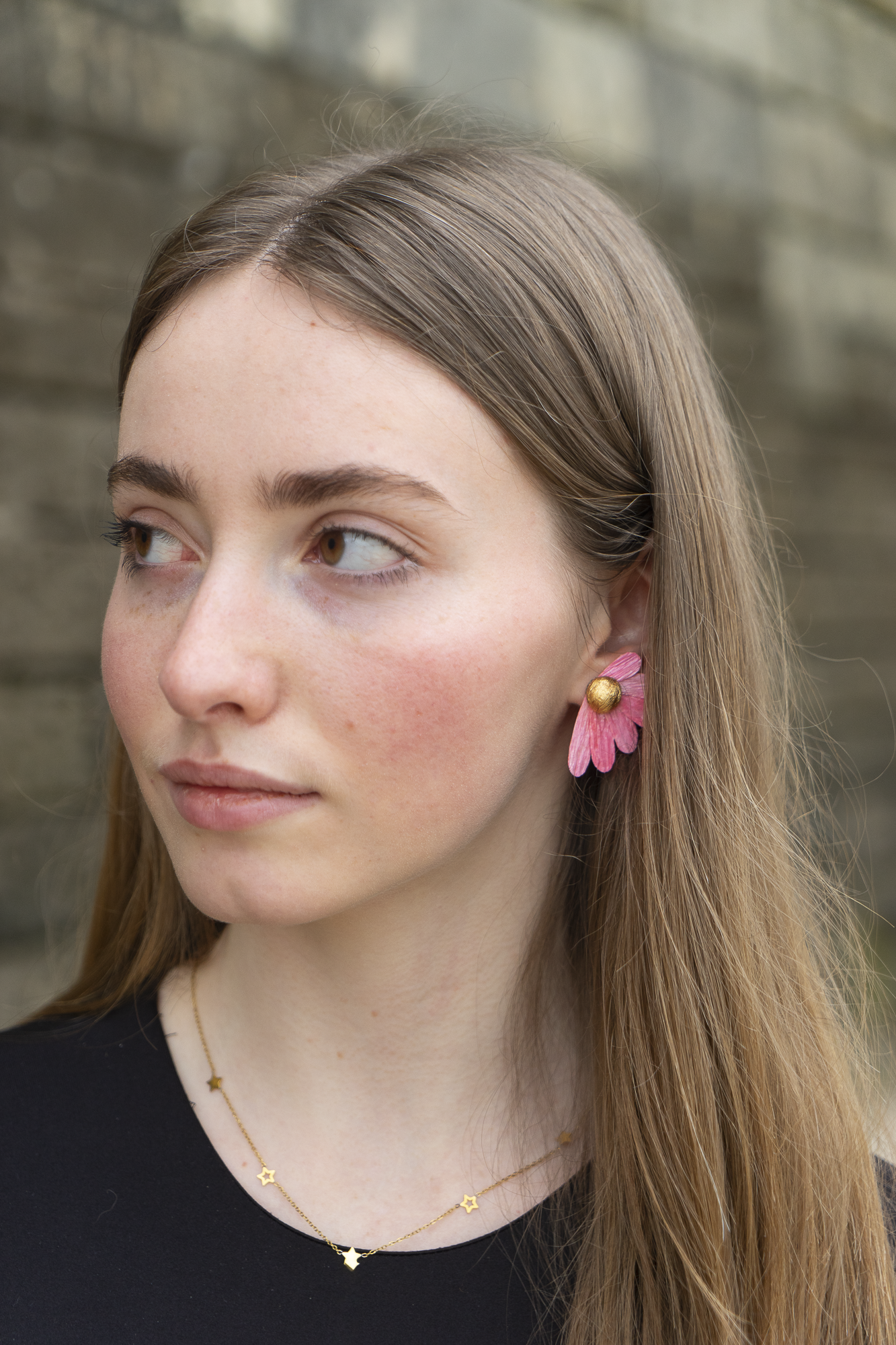 Femme portant des boucles d’oreilles, Puces Pâquerrettes rose, Tourmaline, en papier crépon fait main, bijoux floraux artisanaux fabriqués par Maison Tessier.