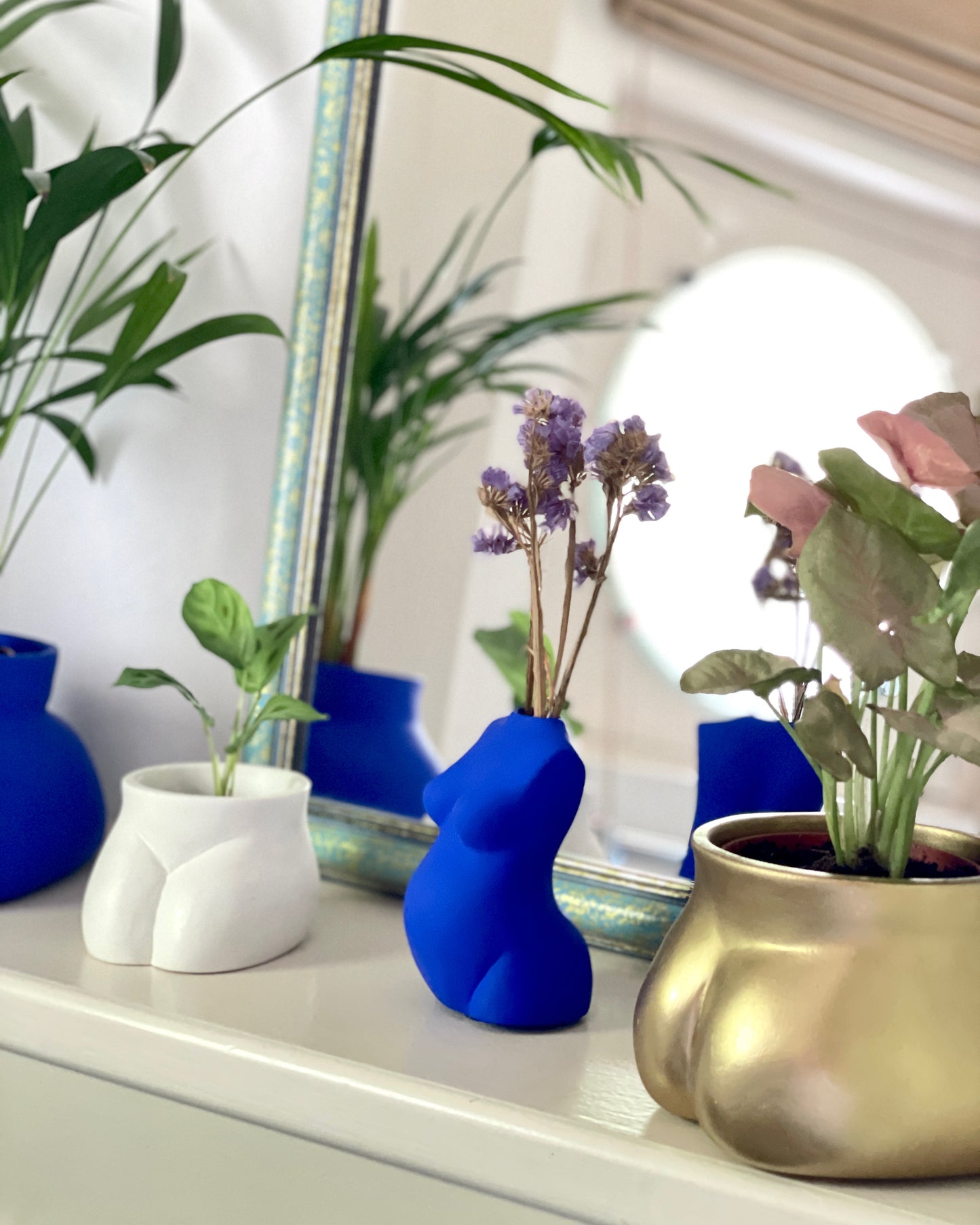 Cache pot Mini Fessier de Maison Tessier, face avant, pubis, de couleur Lune avec une plante, à coté du vase Maman et de pot Fessier doré et Bleu Klein, face à un miroir