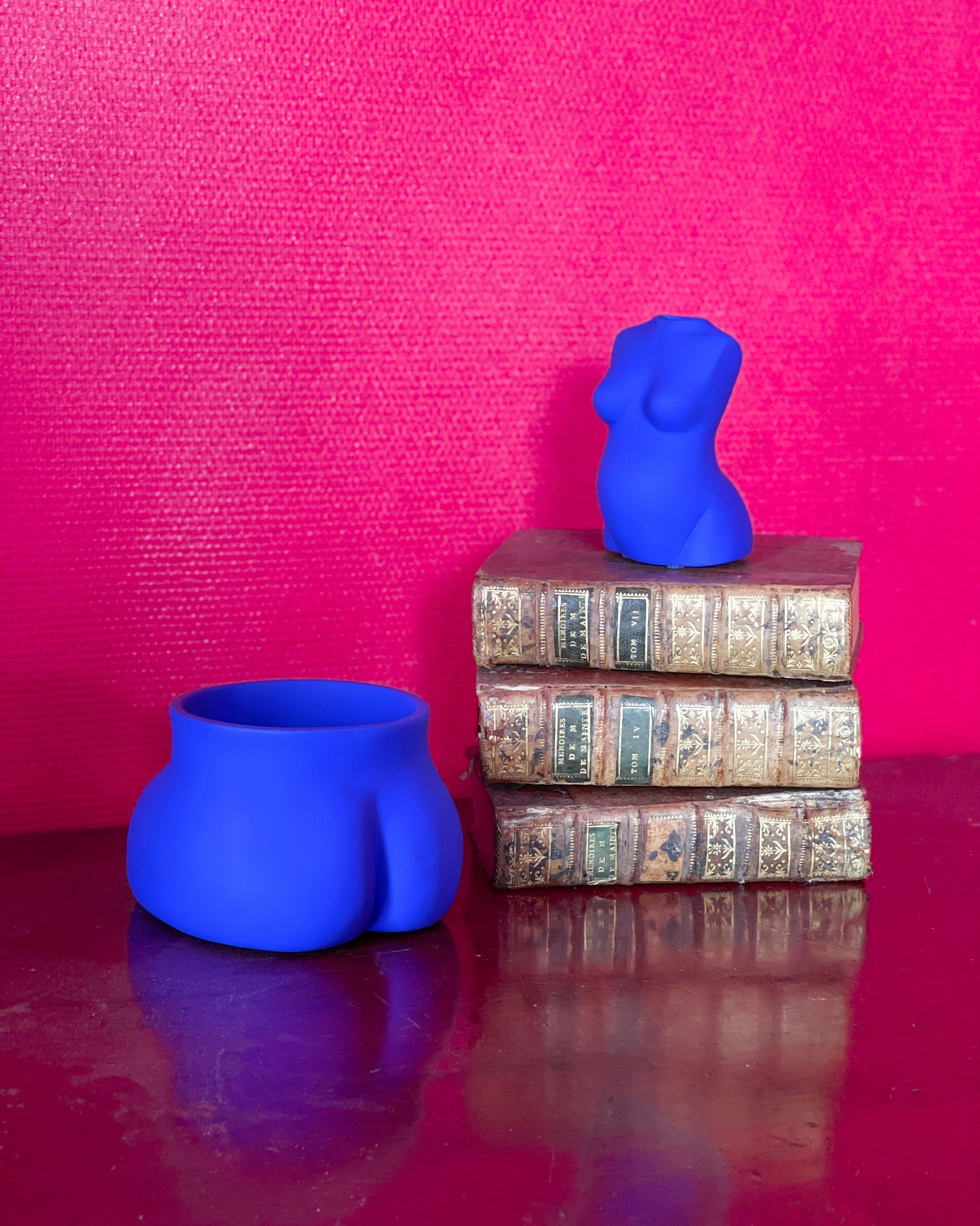 Un Petit Fessier Bleu Klein de Maison Tessier avec le vase Maman sur une pile de vieux livres sur fond rose fushia