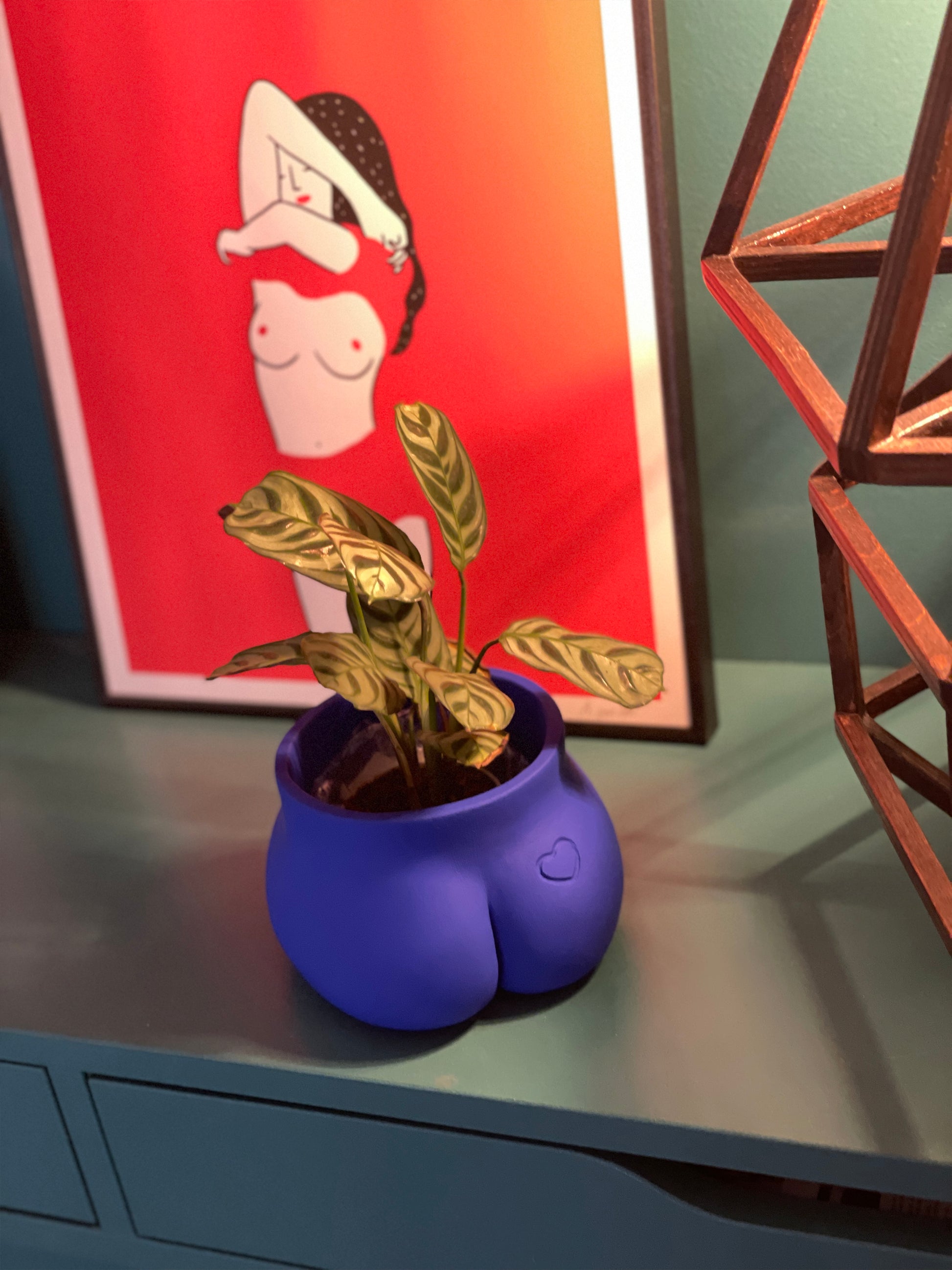 Exemple de gravure personnalisée sur la fesse du pot Petit Fessier de Maison Tessier couleur Bleu Klein, devant une illustration d’Agathe Sorlet et une lampe