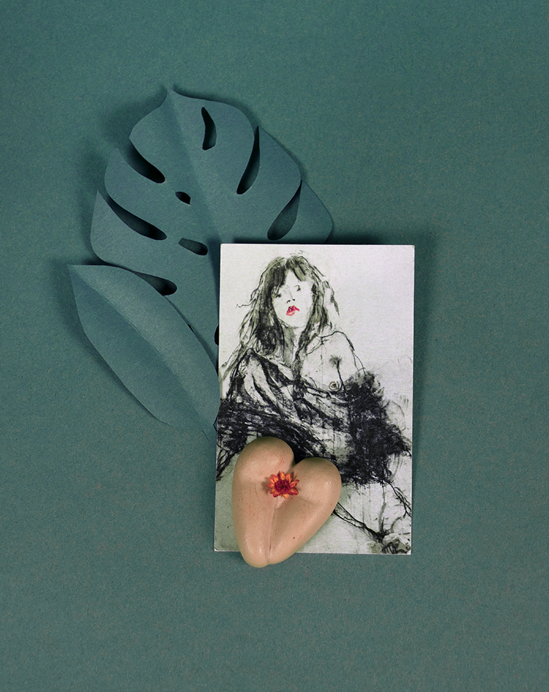 Coeur à nu de Maison Tessier, café, fesses en forme de coeur avec petite fleur corail, sur fond vert émeraude avec feuilles en papier et carte de visite