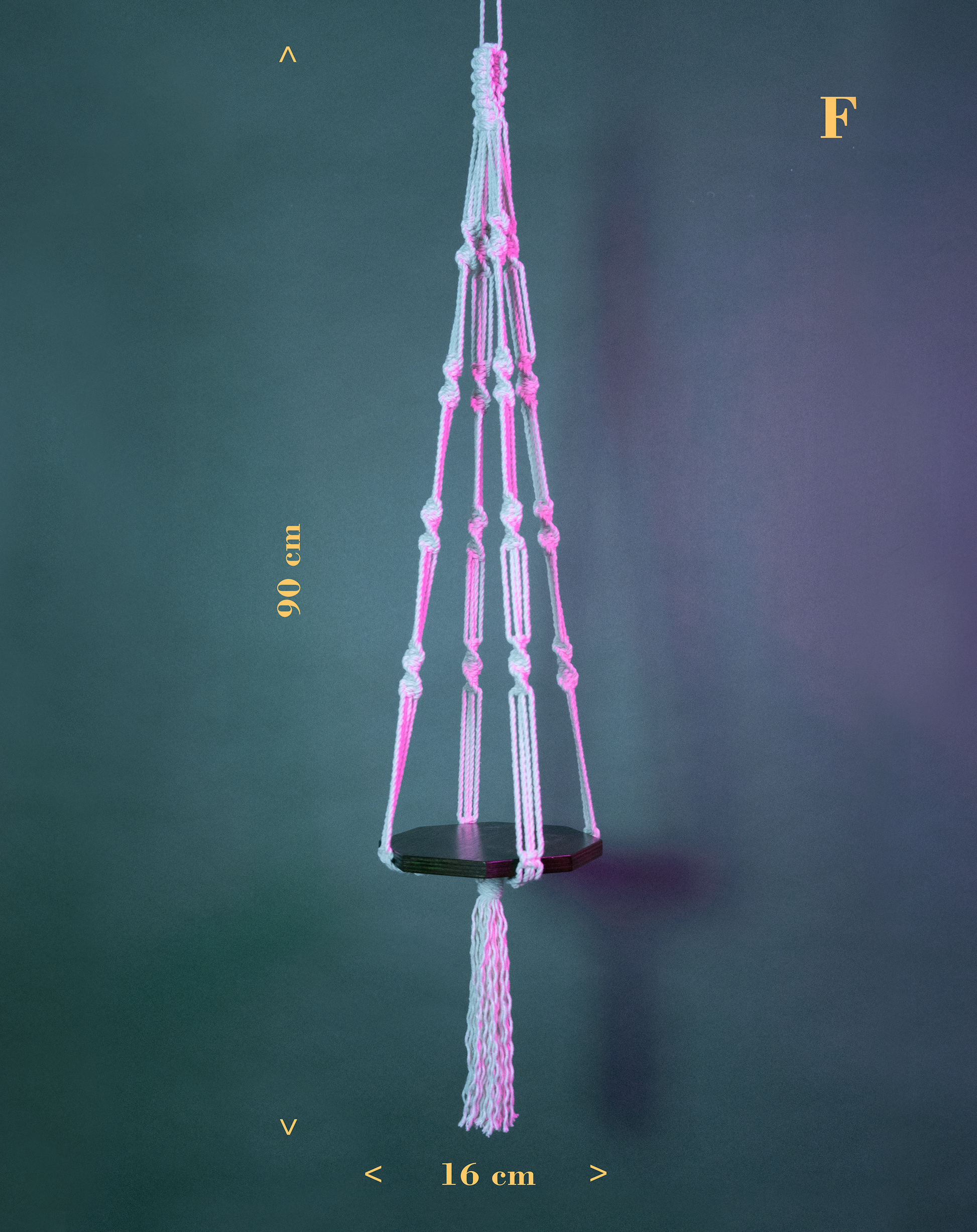 Une suspension en macramé de coton et plateau en bois PLANIUM MAXIMA, de la marque Maison Tessier, derrière un fond bleu avec des reflets de lumière rose