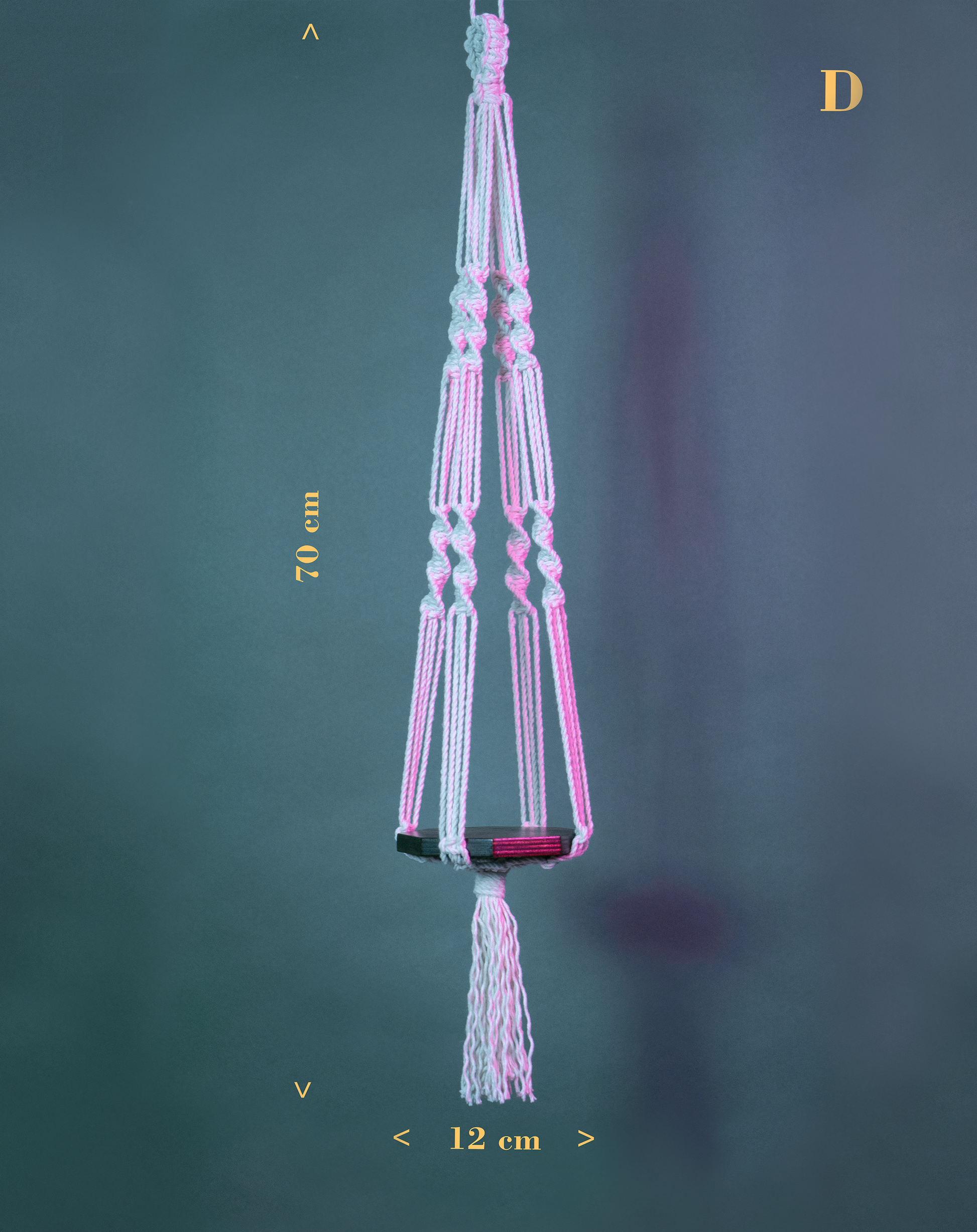 Une suspension en macramé de coton et plateau en bois PLANIUM MINIMA, de la marque Maison Tessier, derrière un fond bleu avec des reflets de lumière rose