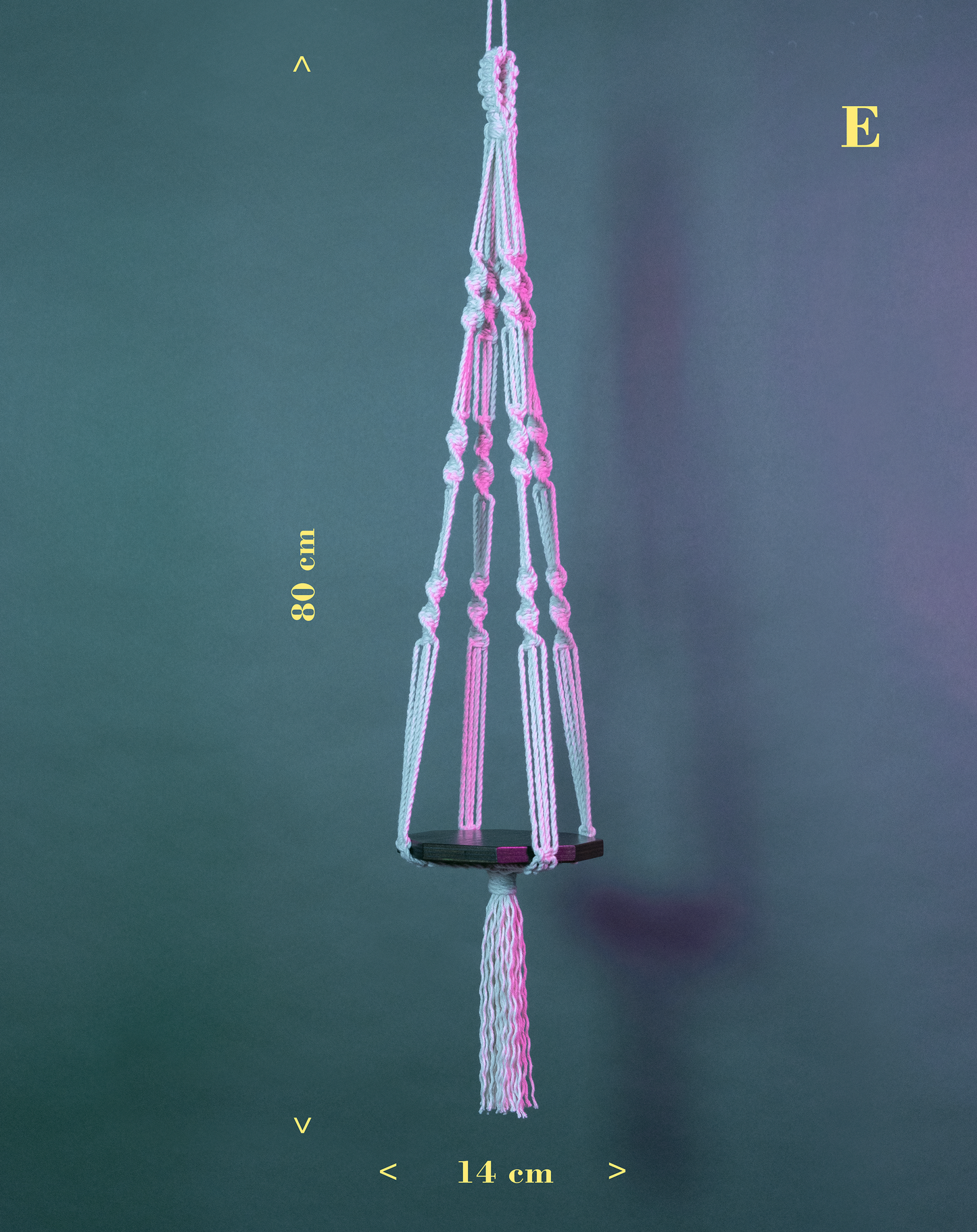 Une suspension en macramé de coton et plateau en bois PLANIUM PUSILLI, de la marque Maison Tessier, derrière un fond bleu avec des reflets de lumière rose