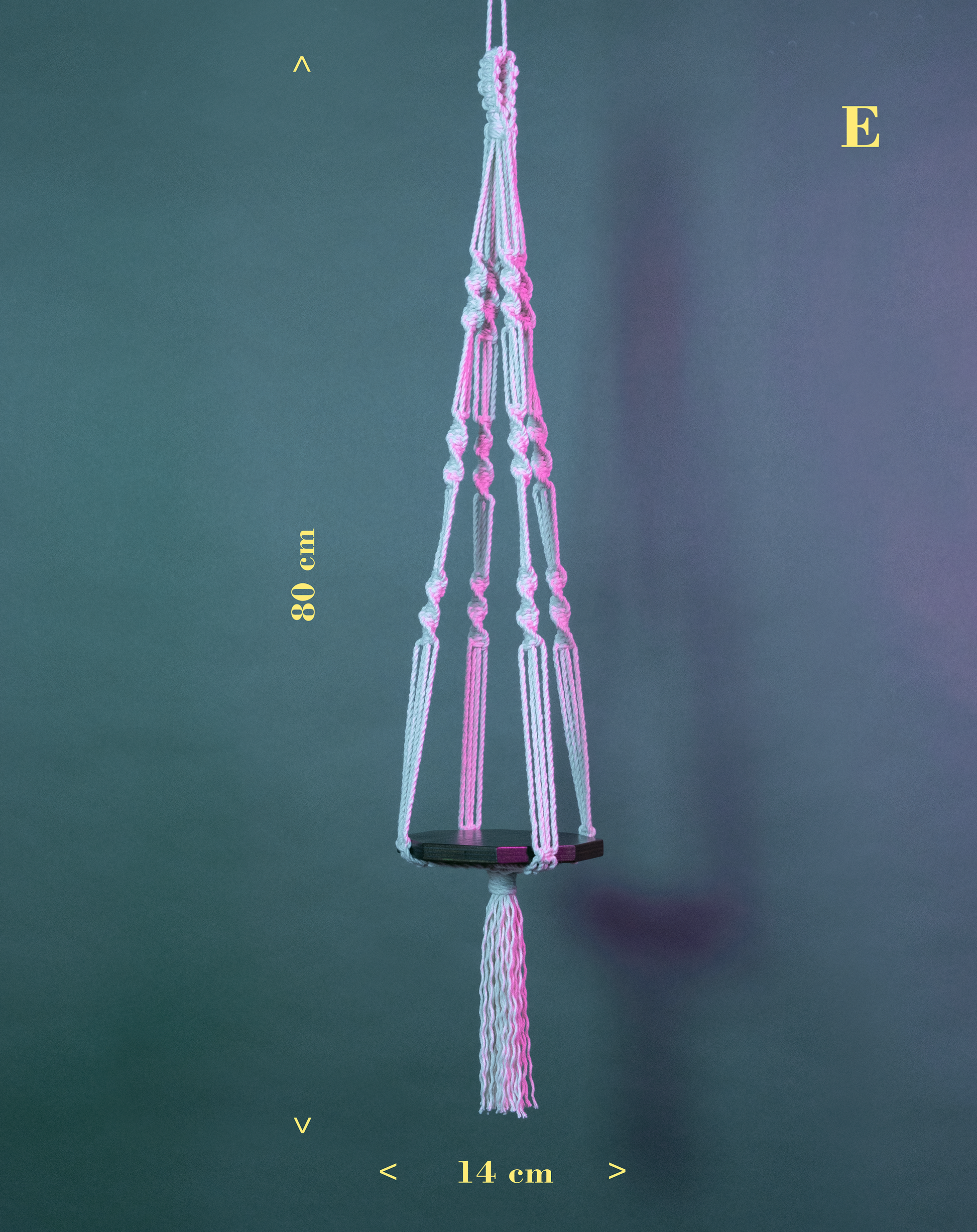 Une suspension en macramé de coton et plateau en bois PLANIUM PUSILLI, de la marque Maison Tessier, derrière un fond bleu avec des reflets de lumière rose