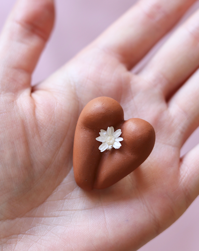 Coeur à nu de Maison Tessier, chocolat, fesses en forme de coeur avec petite fleur blanche, sur une main