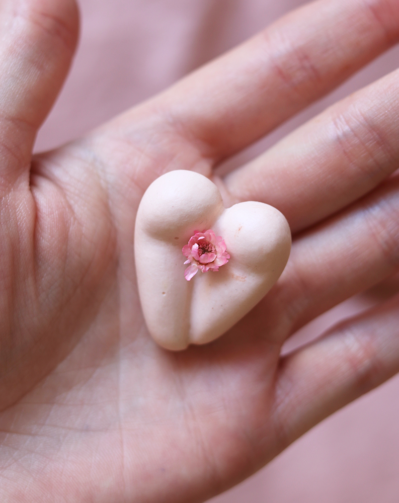 Coeur à nu de Maison Tessier, crème, fesses en forme de coeur avec petite fleur rose, sur une main