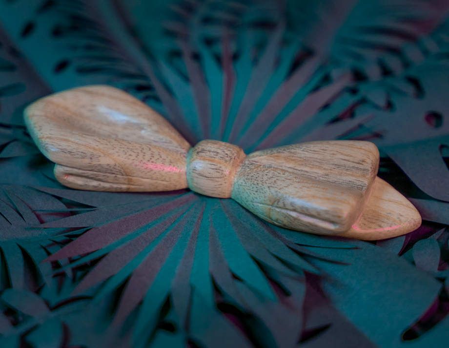 Noeud papillon en bois Maison Tessier en Frêne sur fond de feuilles tropicales en papier, vue de 3/4