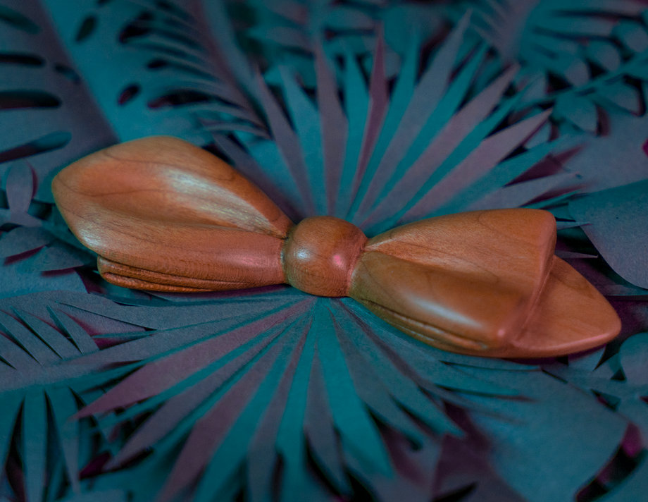 Noeud papillon en bois Maison Tessier en Merisier sur fond de feuilles tropicales en papier, vue de 3/4
