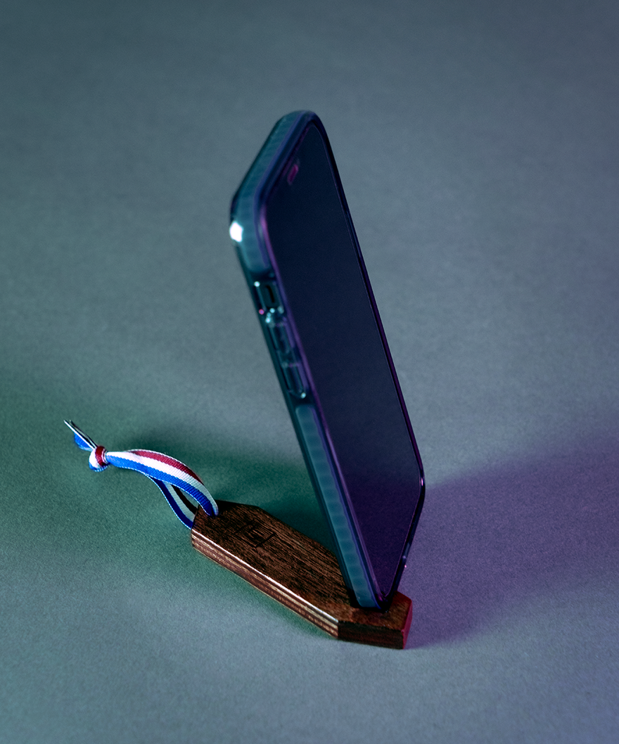 Un téléphone tient de façon verticale grâce au sinemanus de Maison Tessier, il est posé sur un fond photo bleu vert