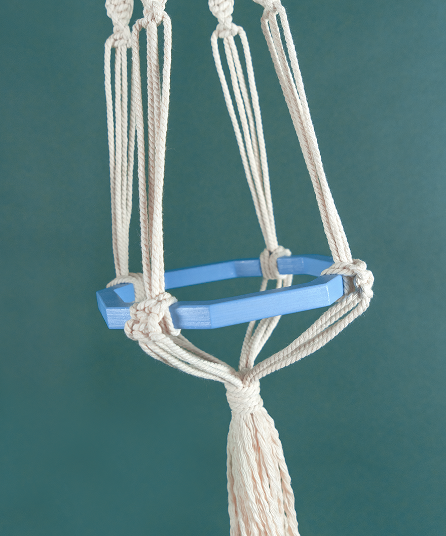 Une suspension en macramé de coton et disque en bois couleur Céleste AUXILIUM MAXIMA, de la marque Maison Tessier, derrière un fond bleu