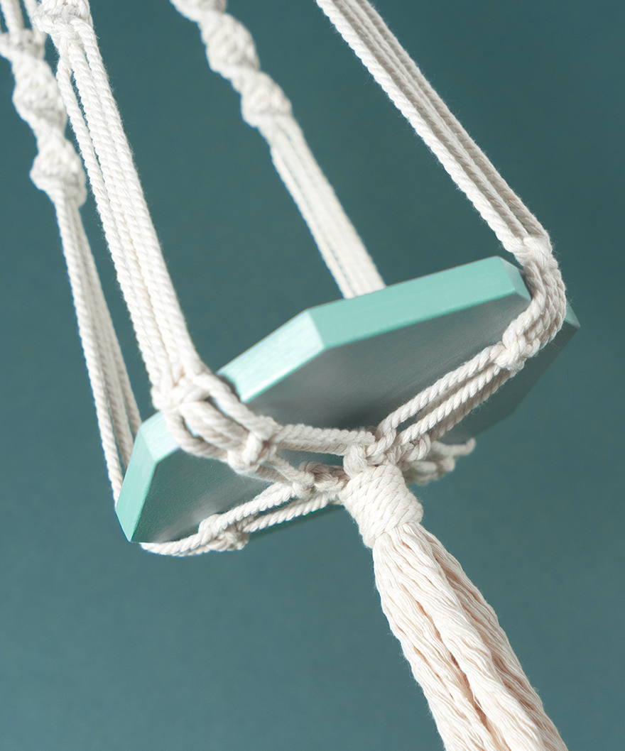 Une suspension en macramé de coton et plateau en bois couleur Céladon PLANIUM MAXIMA, de la marque Maison Tessier, derrière un fond bleu