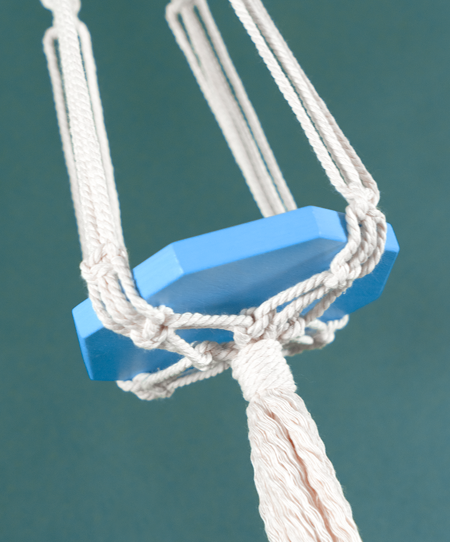 Une suspension en macramé de coton et plateau en bois couleur Céleste PLANIUM MAXIMA, de la marque Maison Tessier, derrière un fond bleu